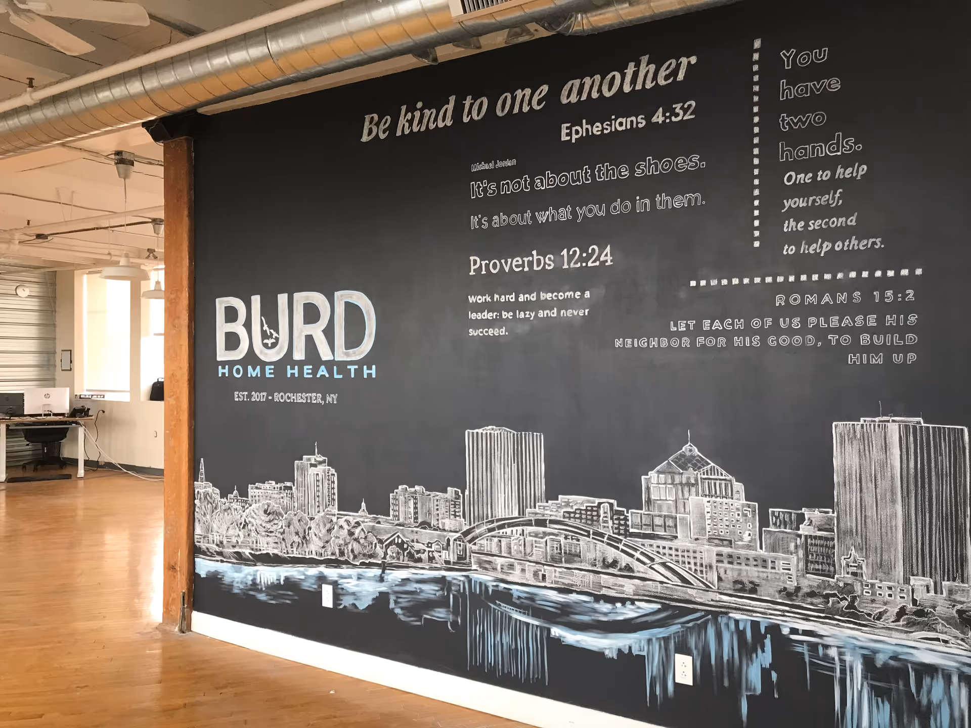 Interior space with a large chalkboard wall mural featuring Burd Home Health branding and city skyline.