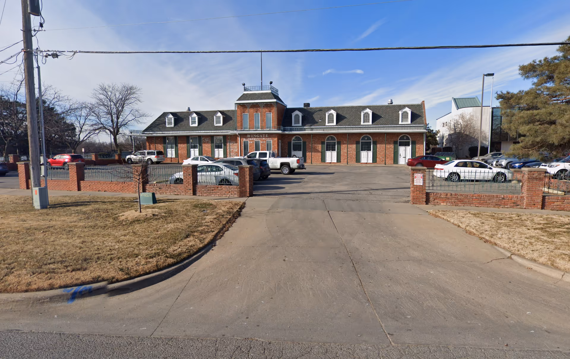 Brick senior care building along a driveway with parked cars and brick pillars.