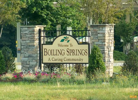 Stone entrance sign reads Welcome To Boiling Springs, A Caring Community, with stone pillars.
