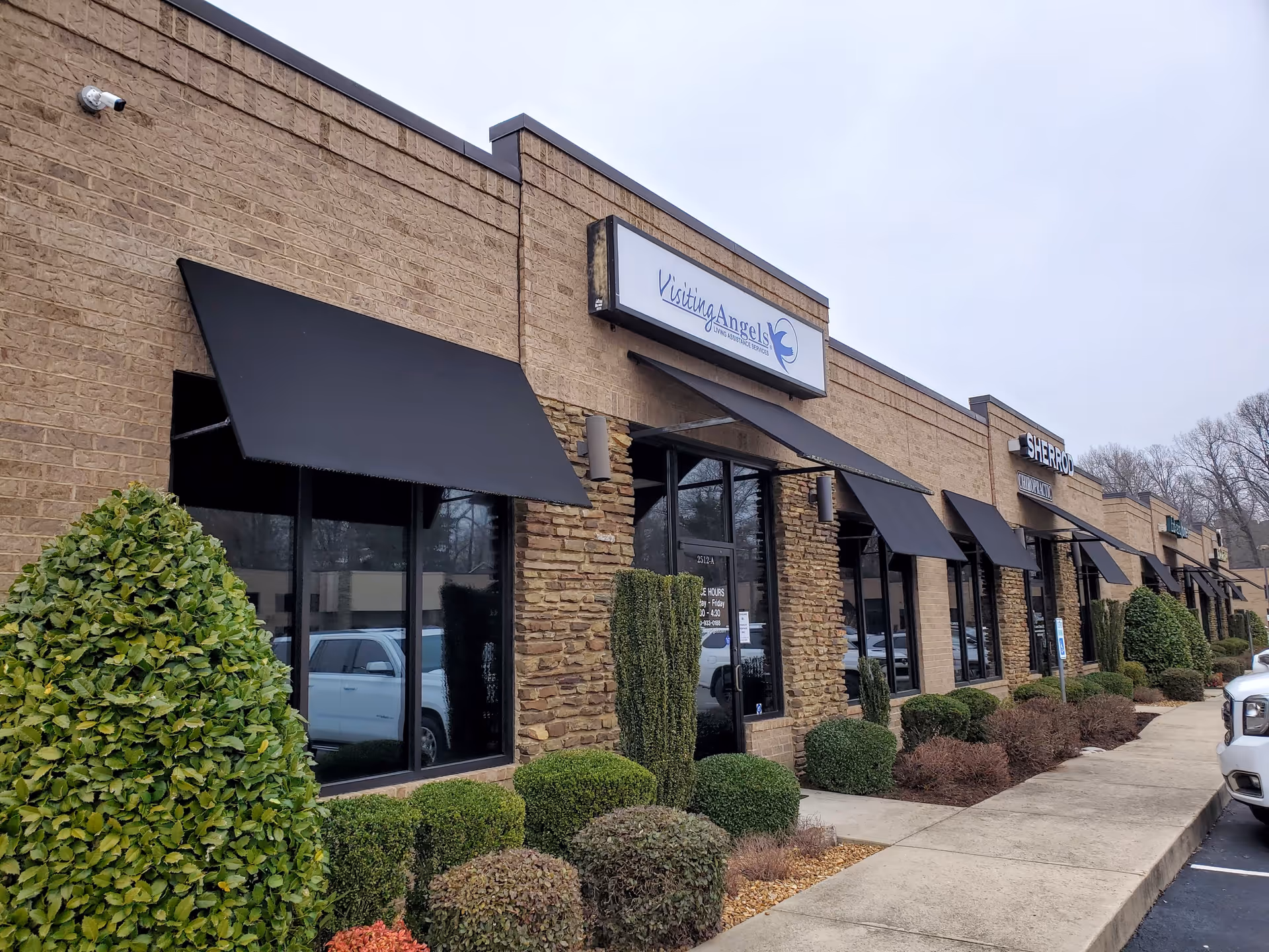 Brick storefronts with black awnings line a sidewalk; Visiting Angels sign visible.