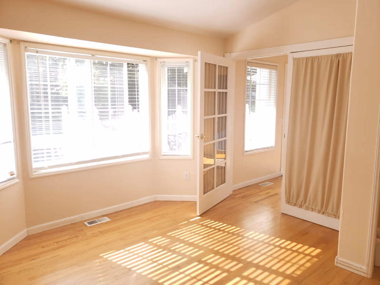 Sunlit beige interior room with large windows, French doors, and a curtain.