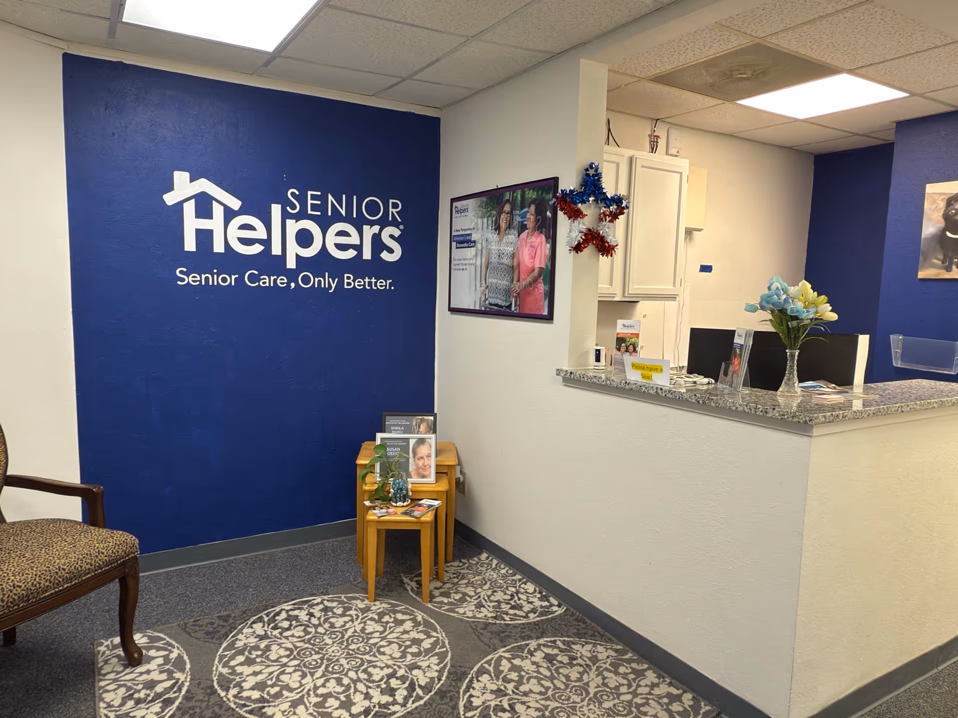 Reception area with blue wall logo Senior Helpers and curved granite front desk.