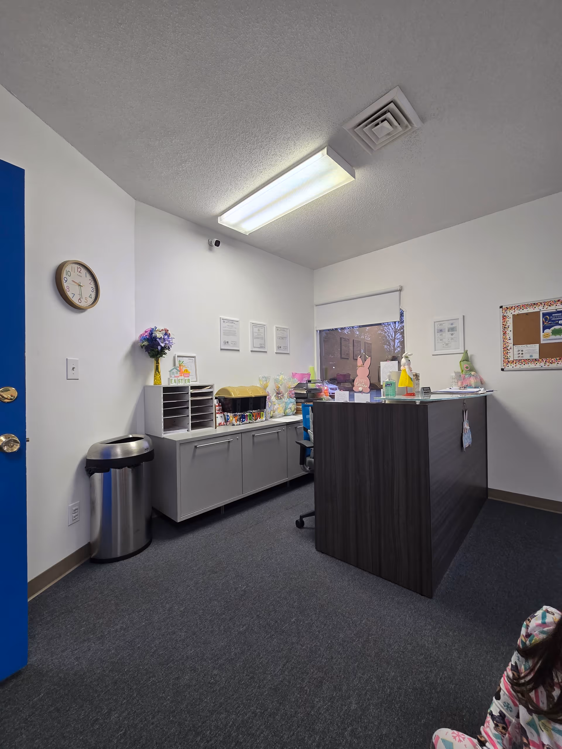 Reception area with a dark wood front desk, cabinets, trash can, clock, and decorations.