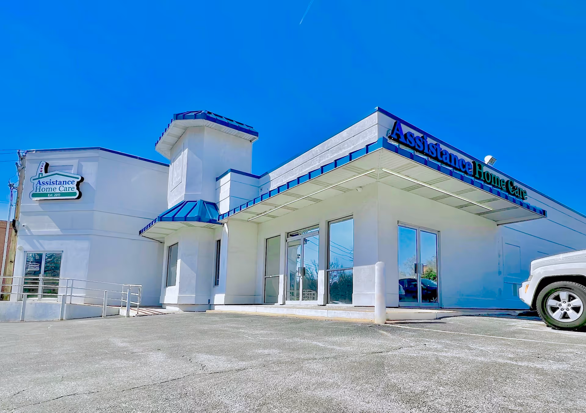 White assisted living facility exterior with blue signage and glass entry doors.