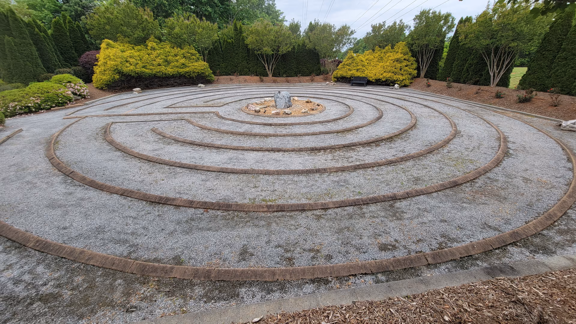 Circular stone labyrinth in a gravel garden with surrounding trees and benches.