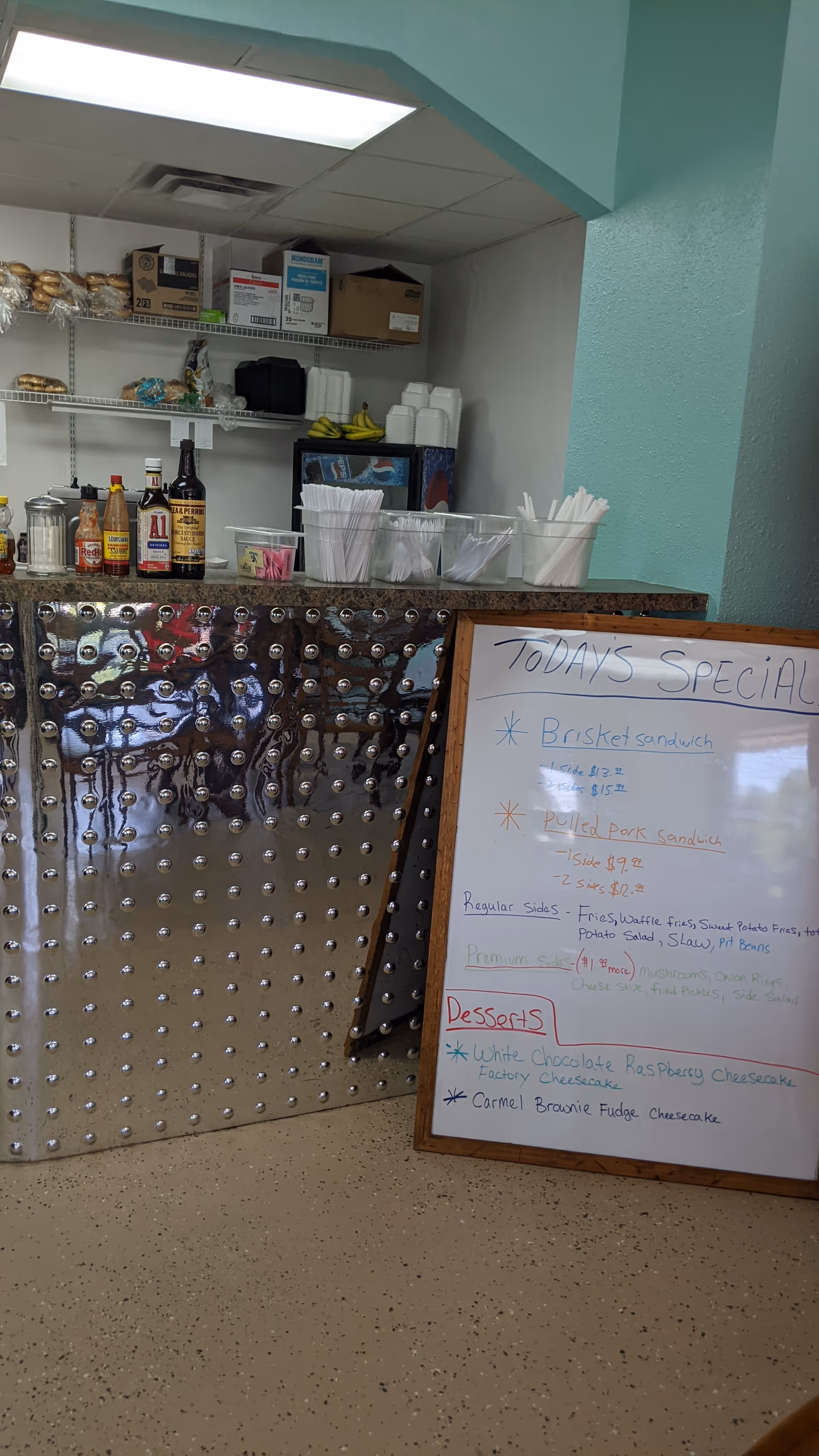Indoor dining counter with bottles, cups, and a whiteboard menu in a cafe-style serving area.