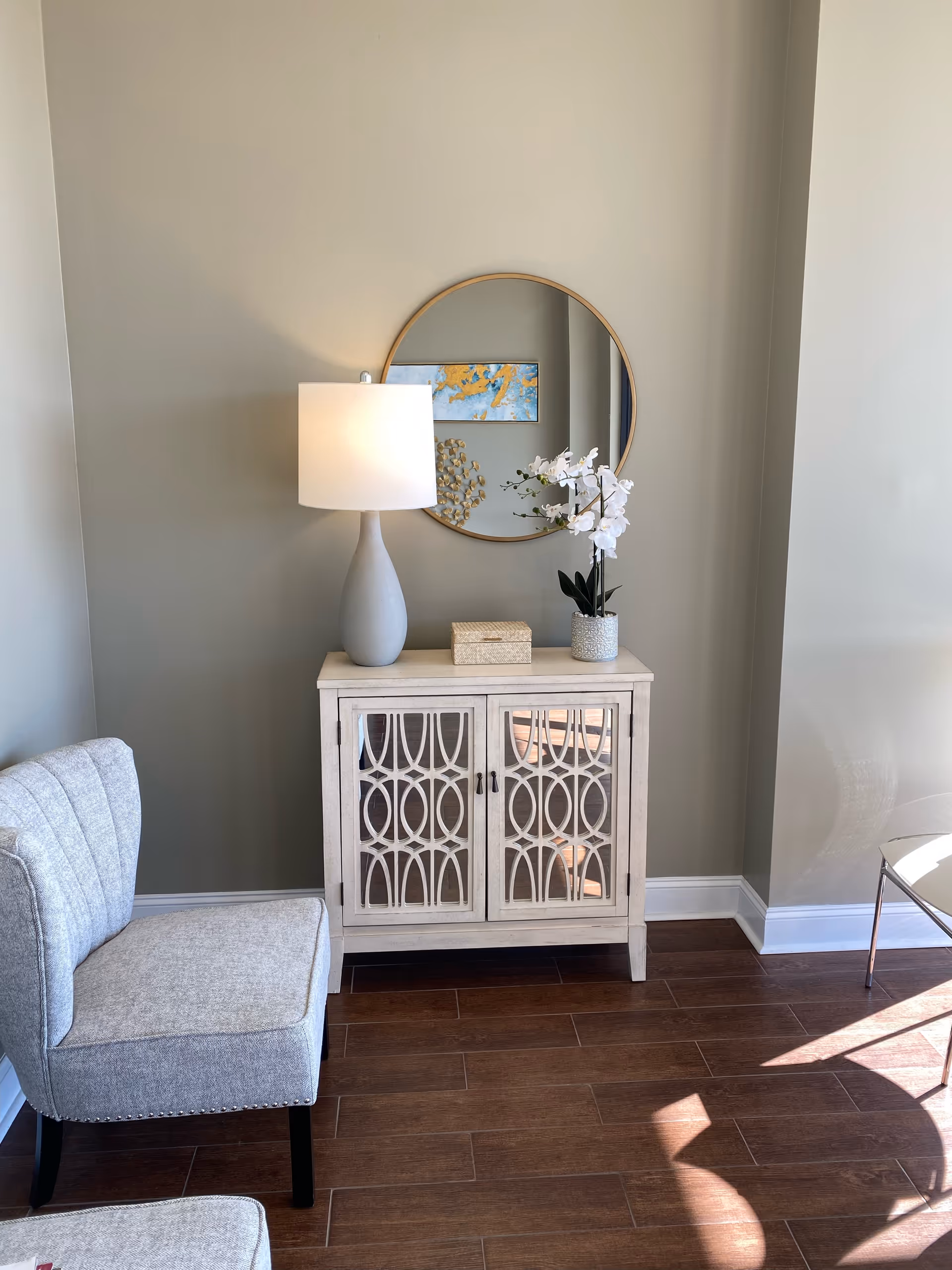 Cozy entry corner with a lamp, orchid, round mirror, and light cabinet.