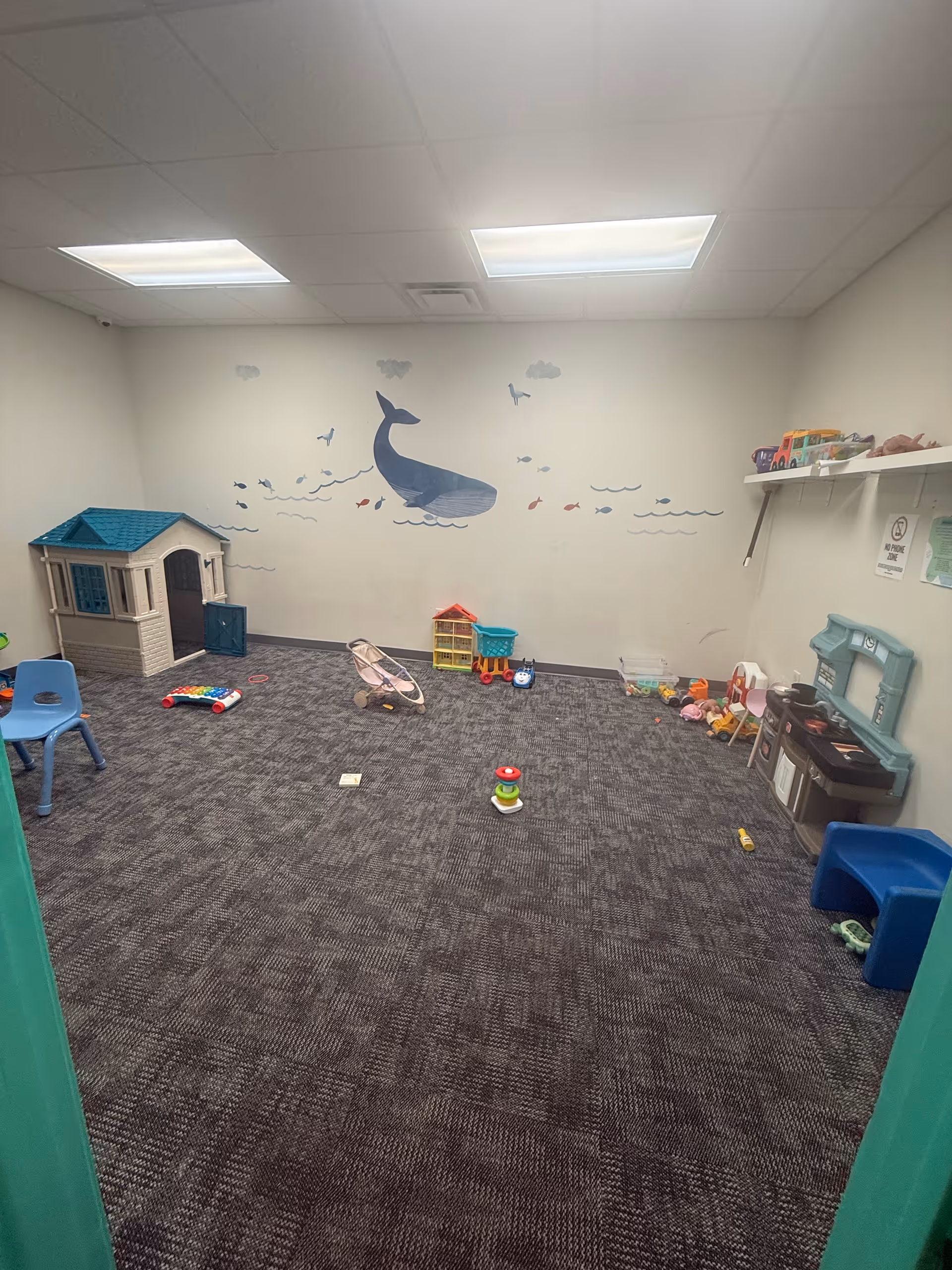 Interior playroom with toys, a small plastic house, and a whale mural on the wall.