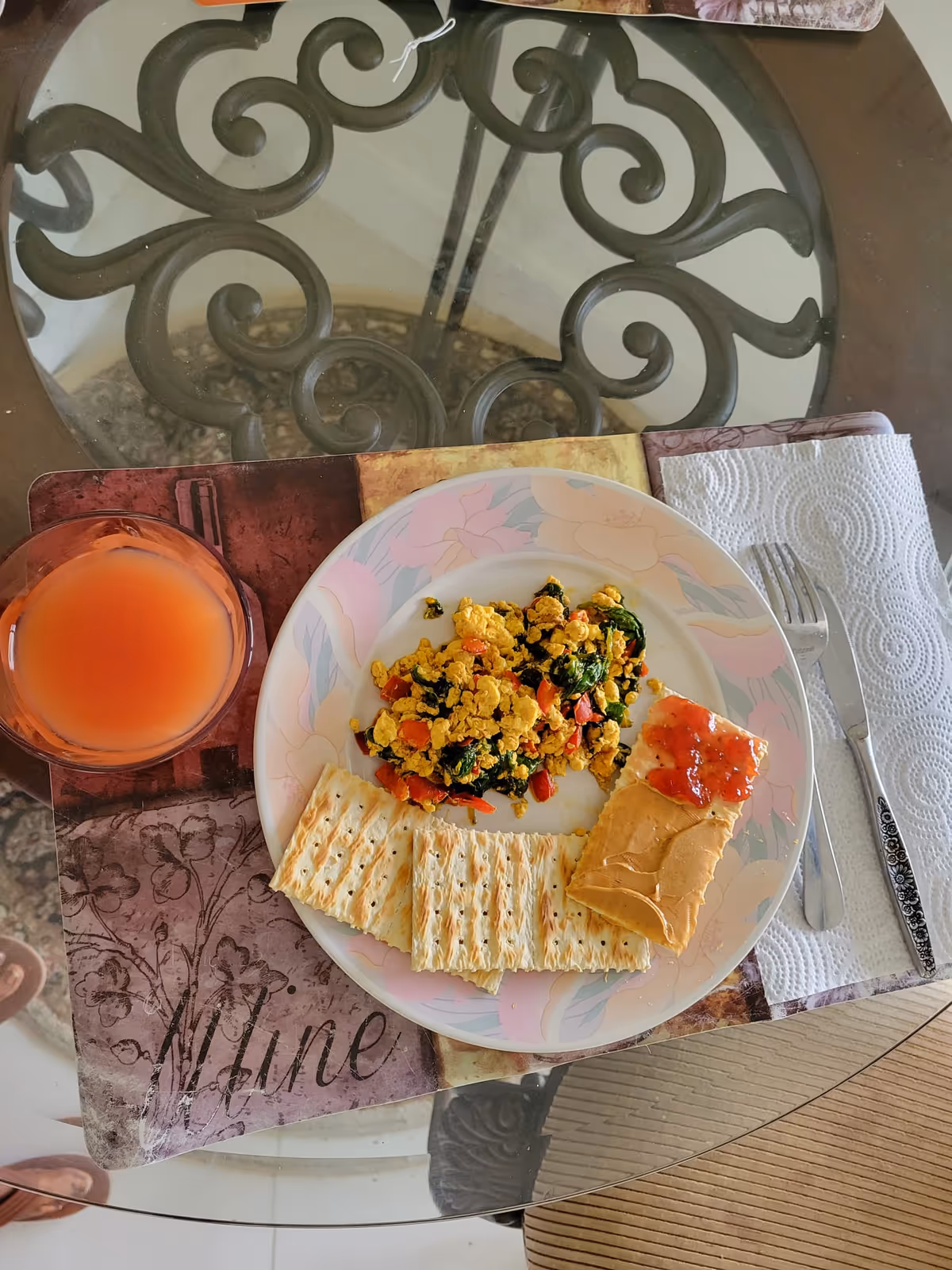 Plate with scrambled eggs and vegetables, crackers, jam, and a glass of orange juice.