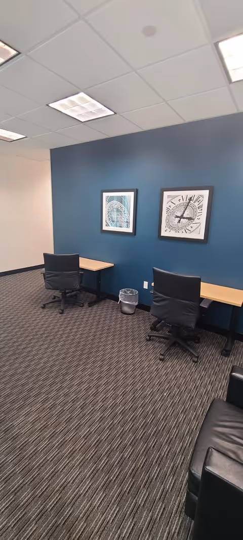 Office-style workspace with two desks, chairs, blue accent wall, and framed artwork.