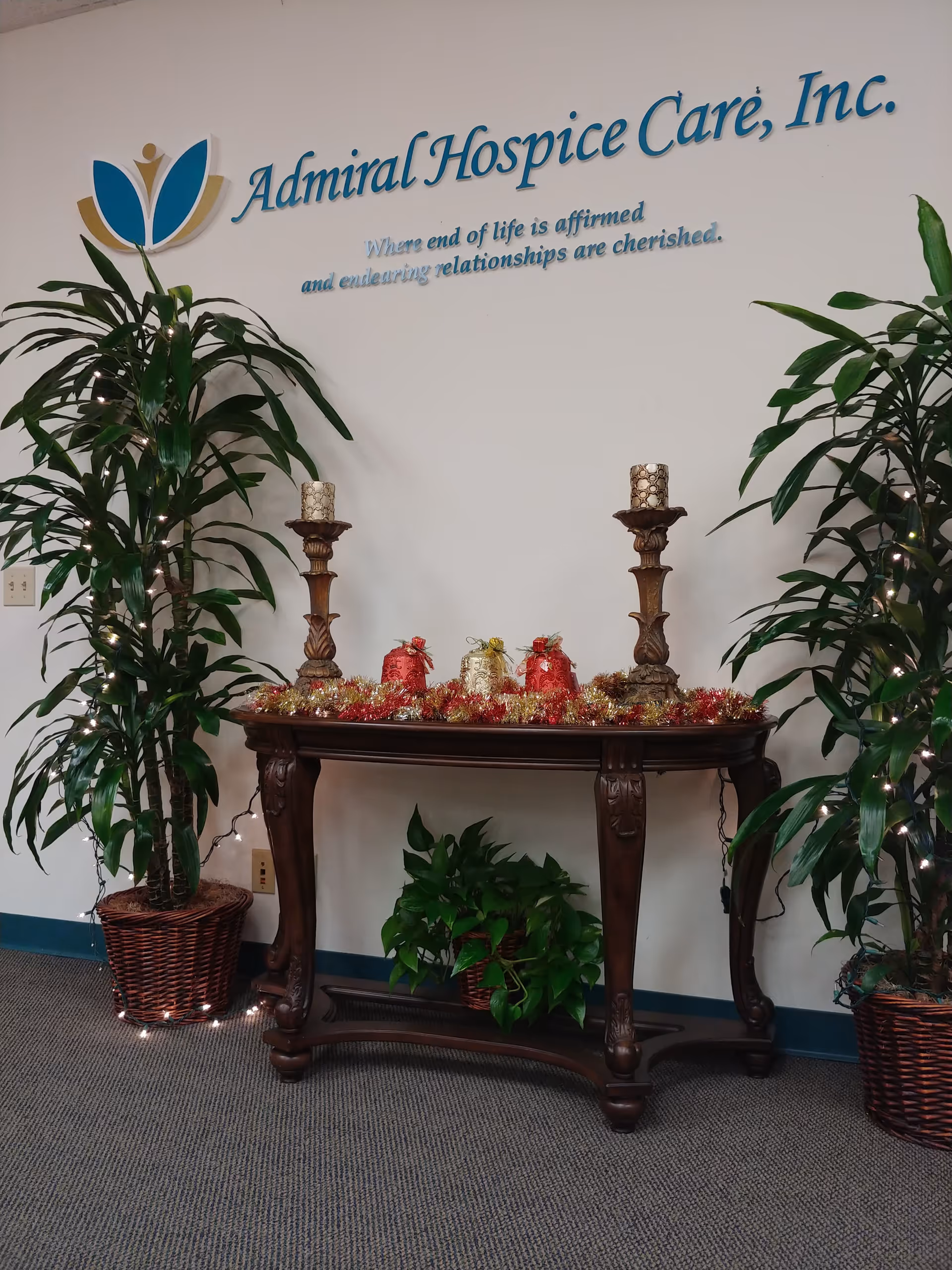 Interior lobby with a wooden console table, plants, candles, and Admiral Hospice Care sign.