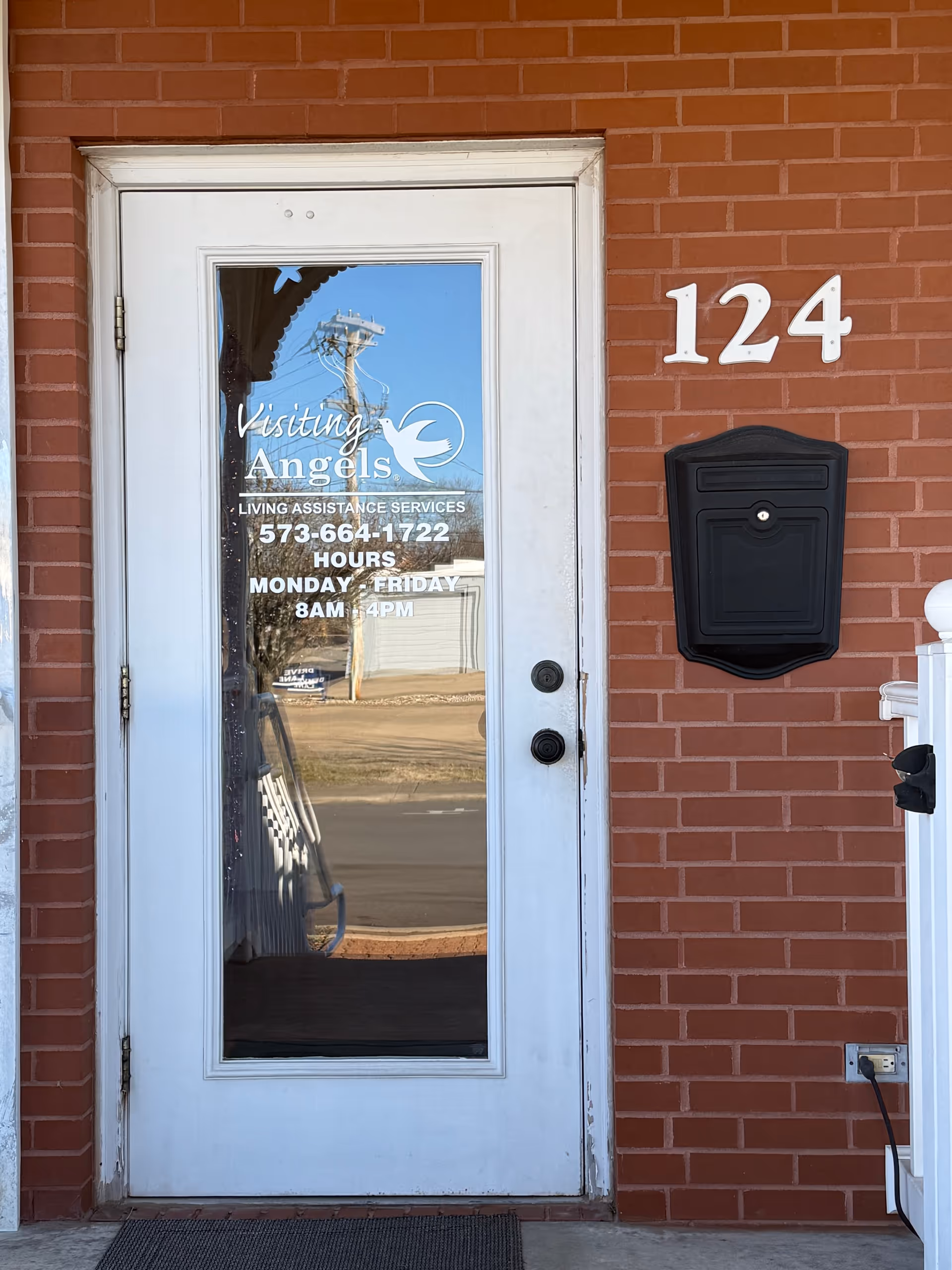 White glass door with Visiting Angels sign, brick building, and the number 124 beside a mailbox.