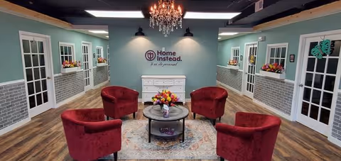 A cozy lounge with teal walls, red chairs, a round table, and a Home Instead logo.
