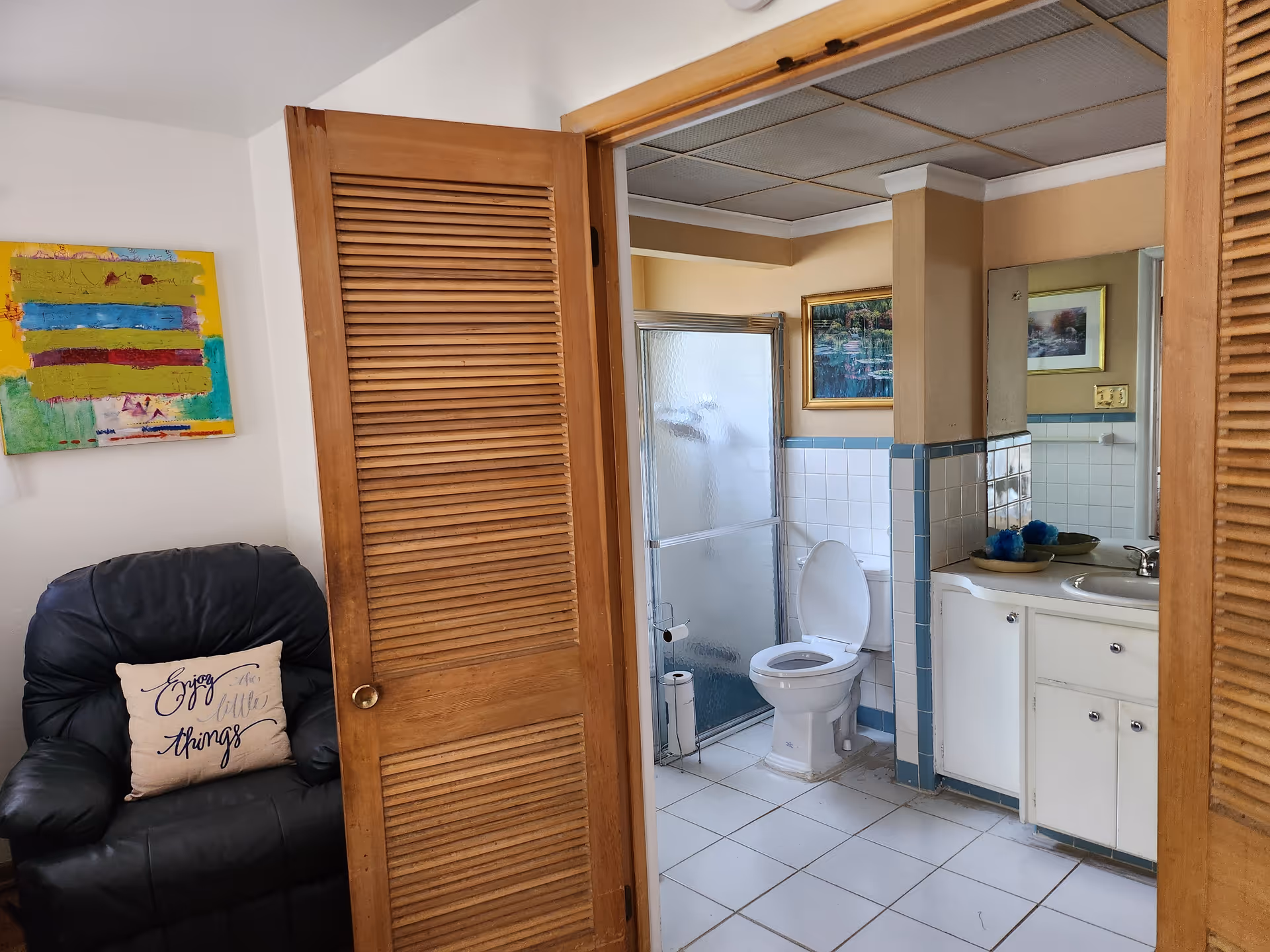 Open doorway reveals a bathroom with toilet, shower, and sink beside a living area.
