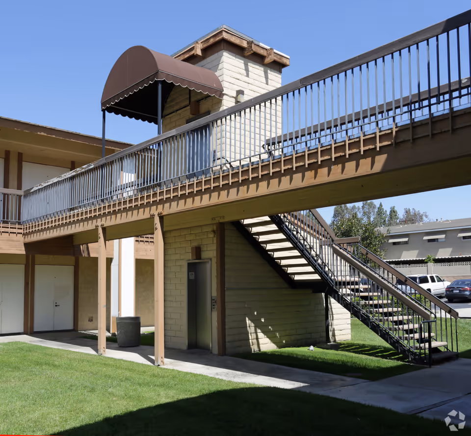 Two-story outdoor walkway with metal railing and stairs beside a beige building.