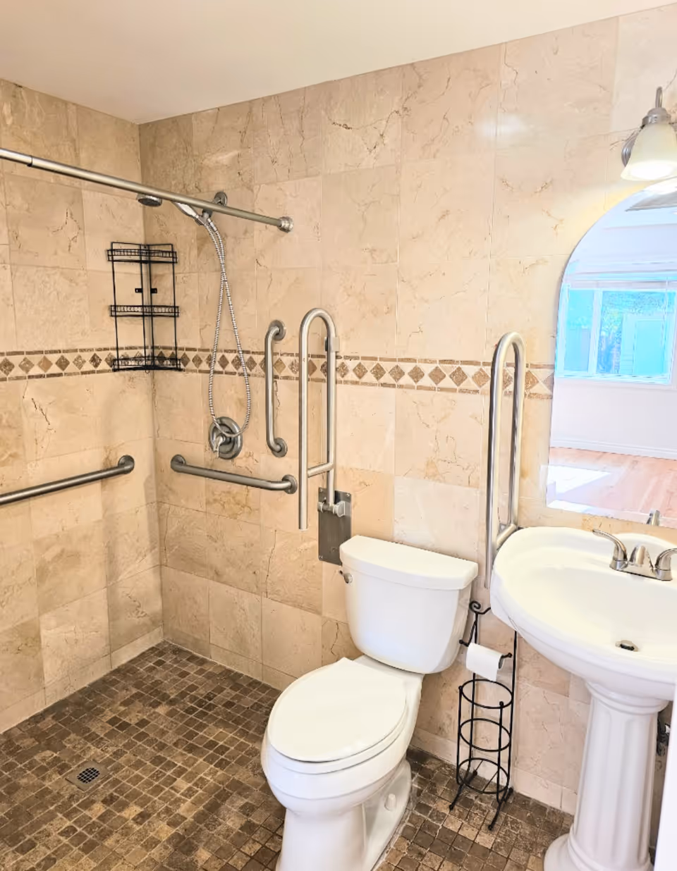 Accessible bathroom with grab bars, toilet, pedestal sink, and tiled shower area.