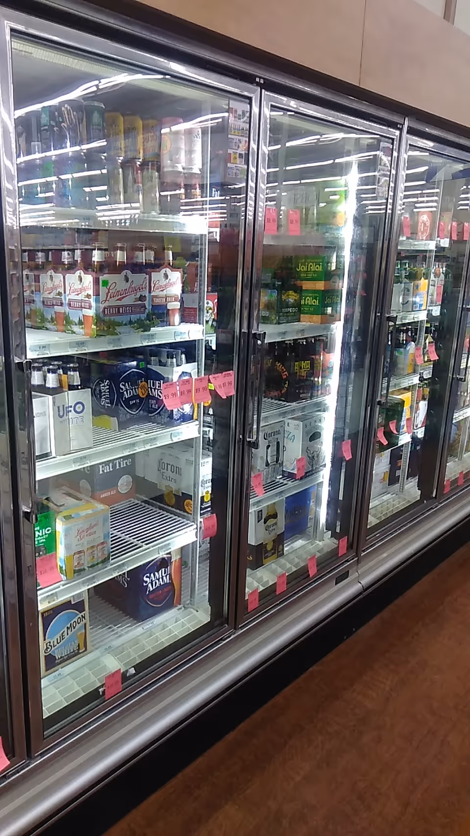 A long refrigerated display with glass doors showing assorted beverages and pink price tags.