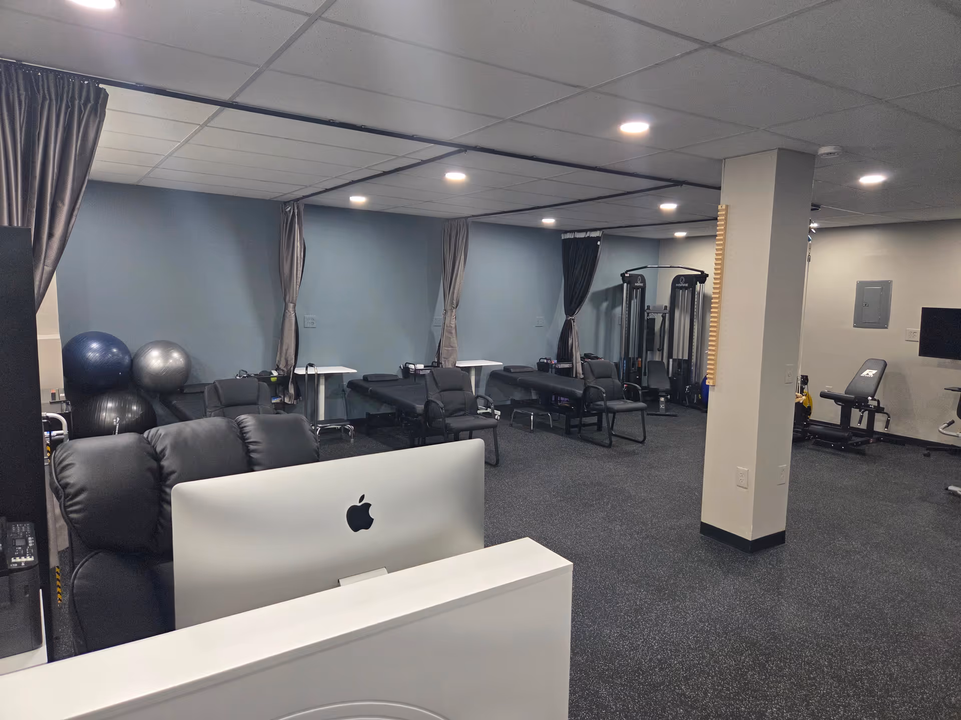 Interior rehabilitation gym with exercise equipment, therapy chairs, and a reception desk.