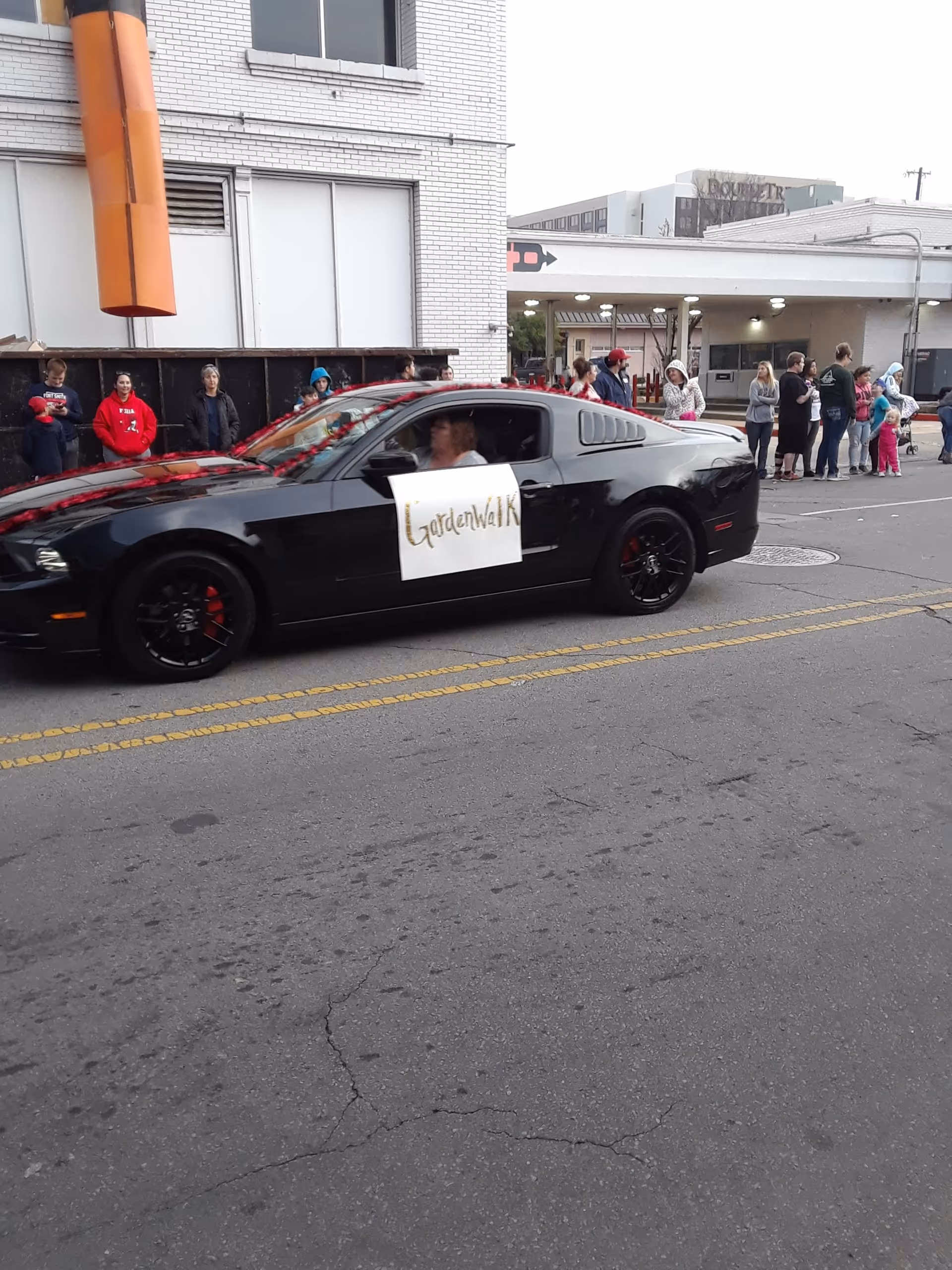 Black sports car drives by as people line a city street outside a building.