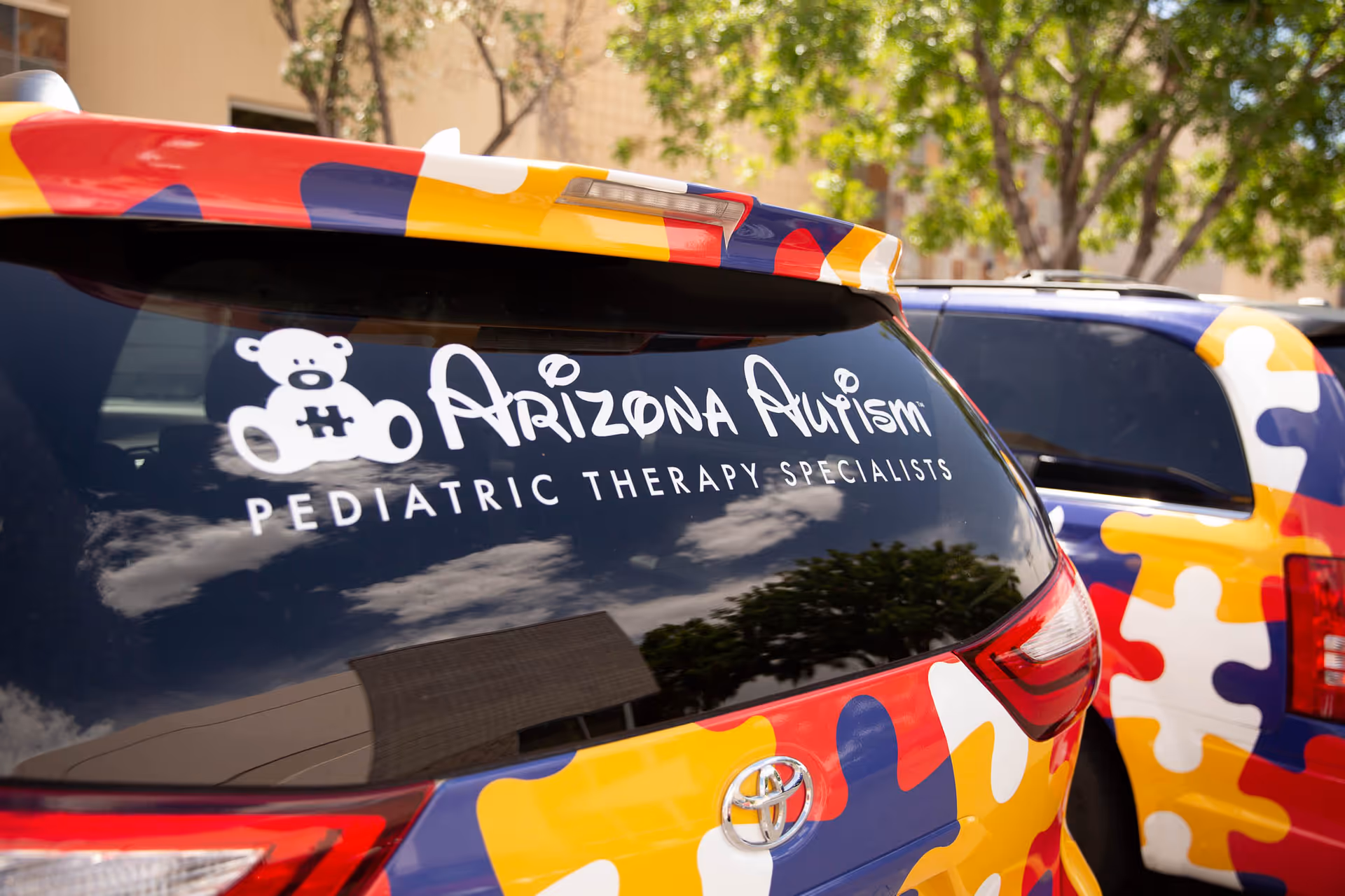 Vibrant puzzle-pattern vans labeled Arizona Autism parked outside.