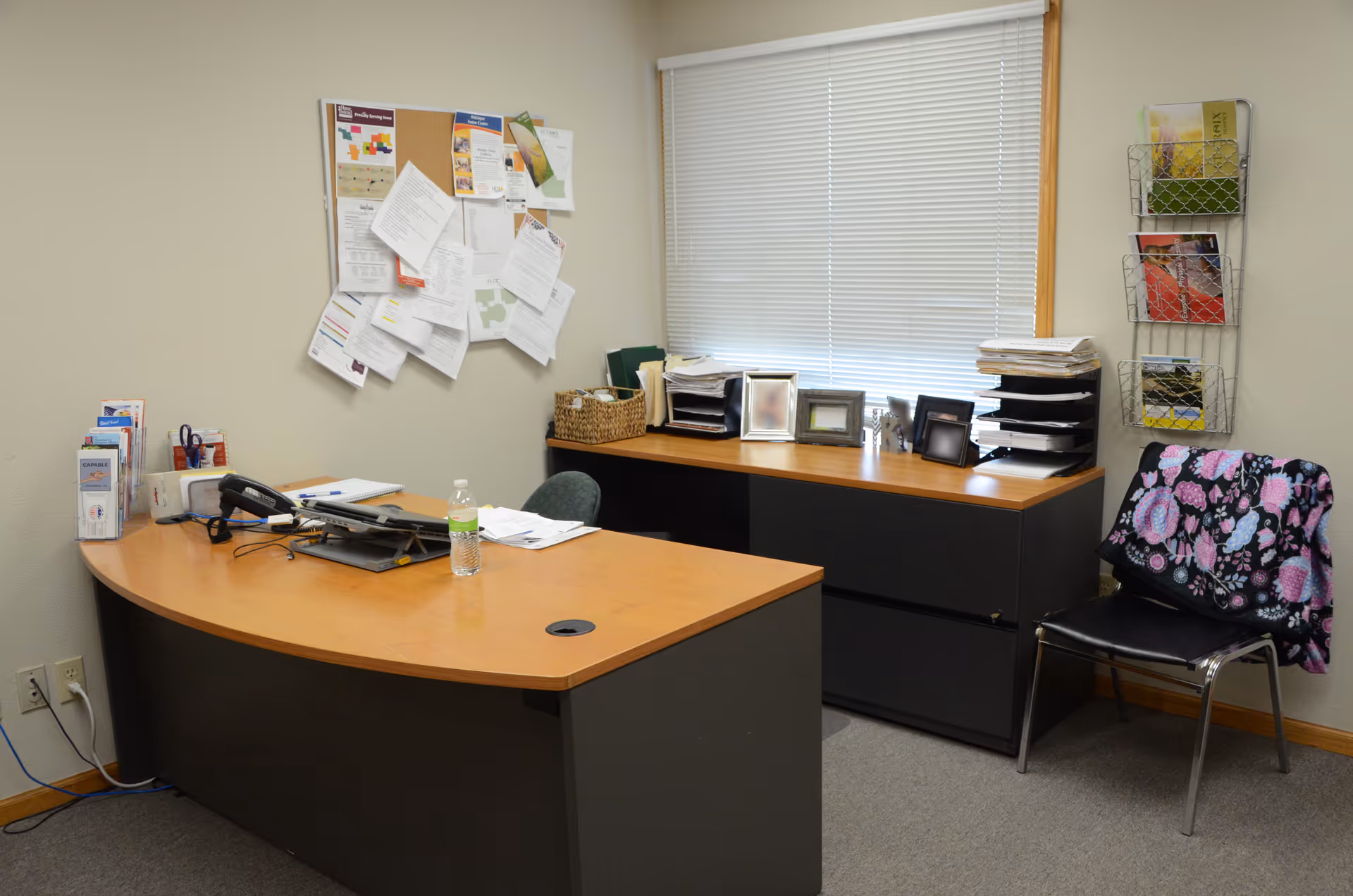Office desk area with bulletin board, files, and window blinds in a senior living facility.