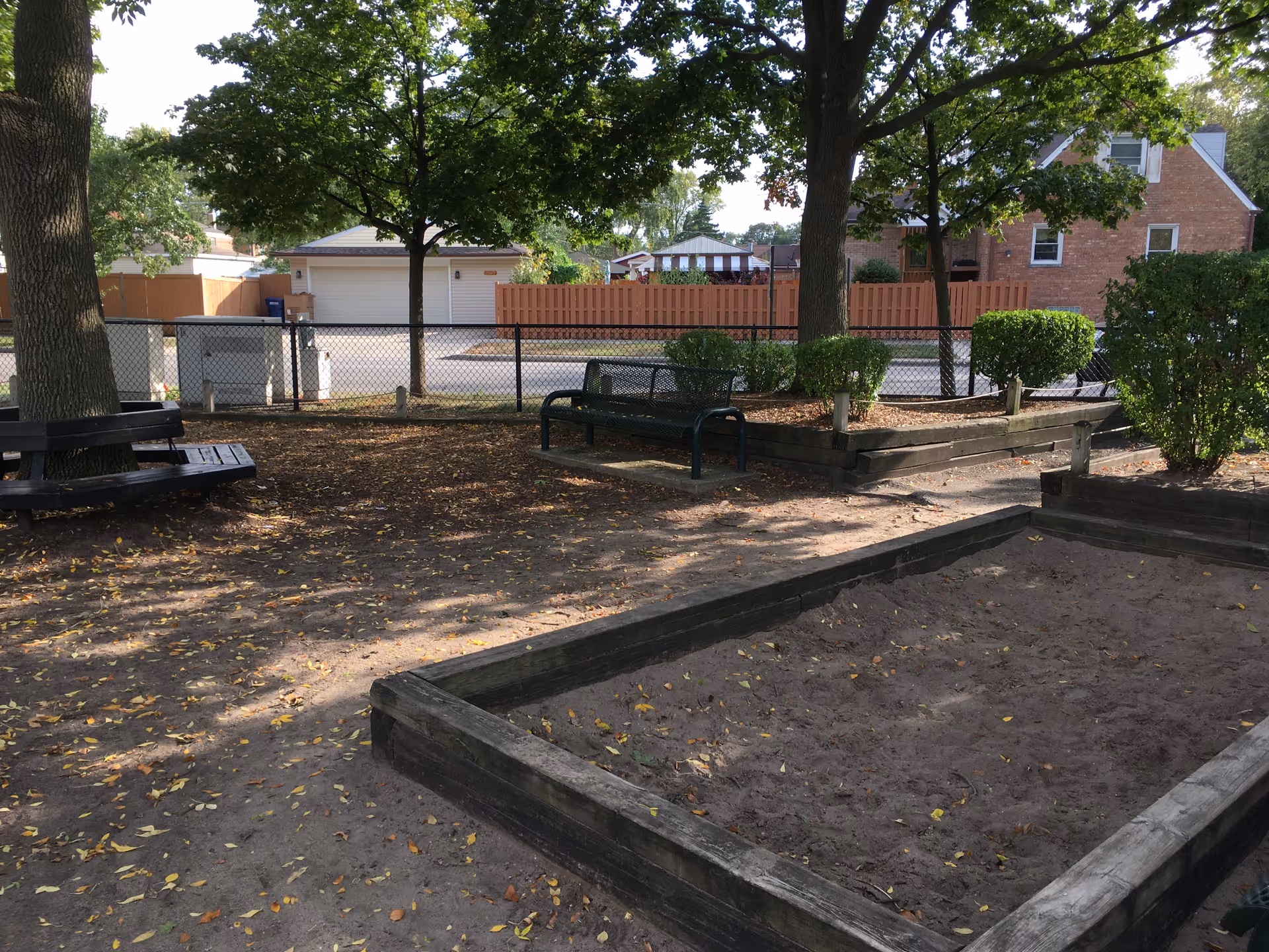 Shaded outdoor area with benches, trees, and raised garden beds.