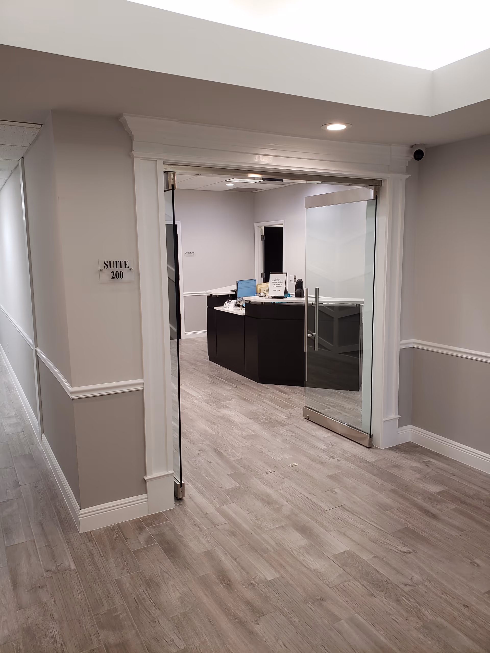 Hallway to a reception area with glass doors and a curved dark desk.