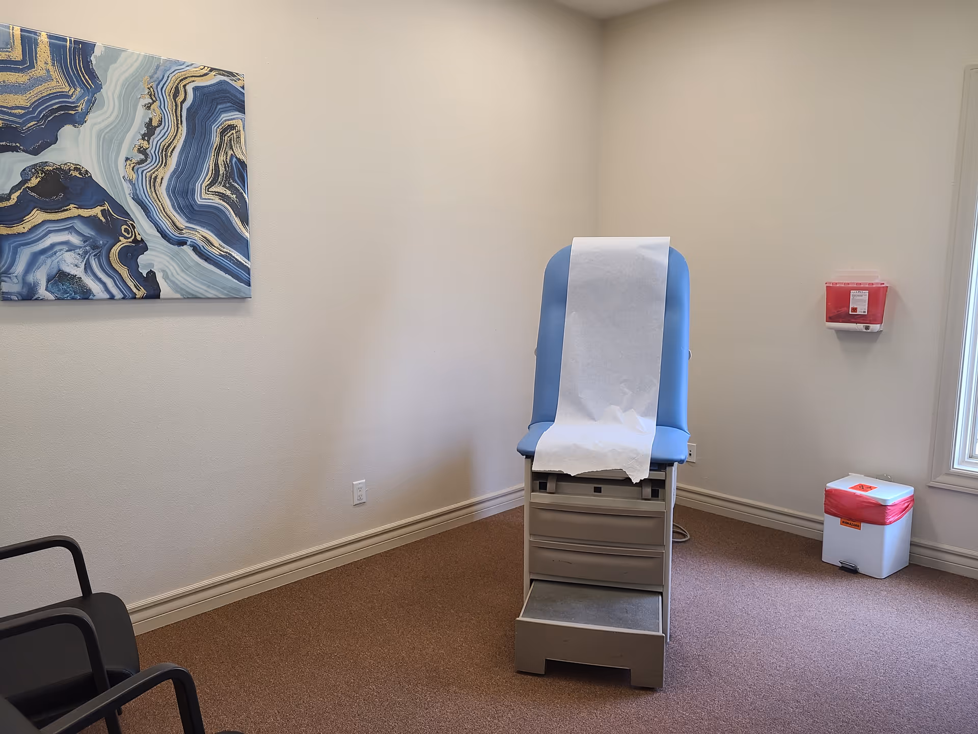 Blue exam chair with paper cover in a small clinic examination room.