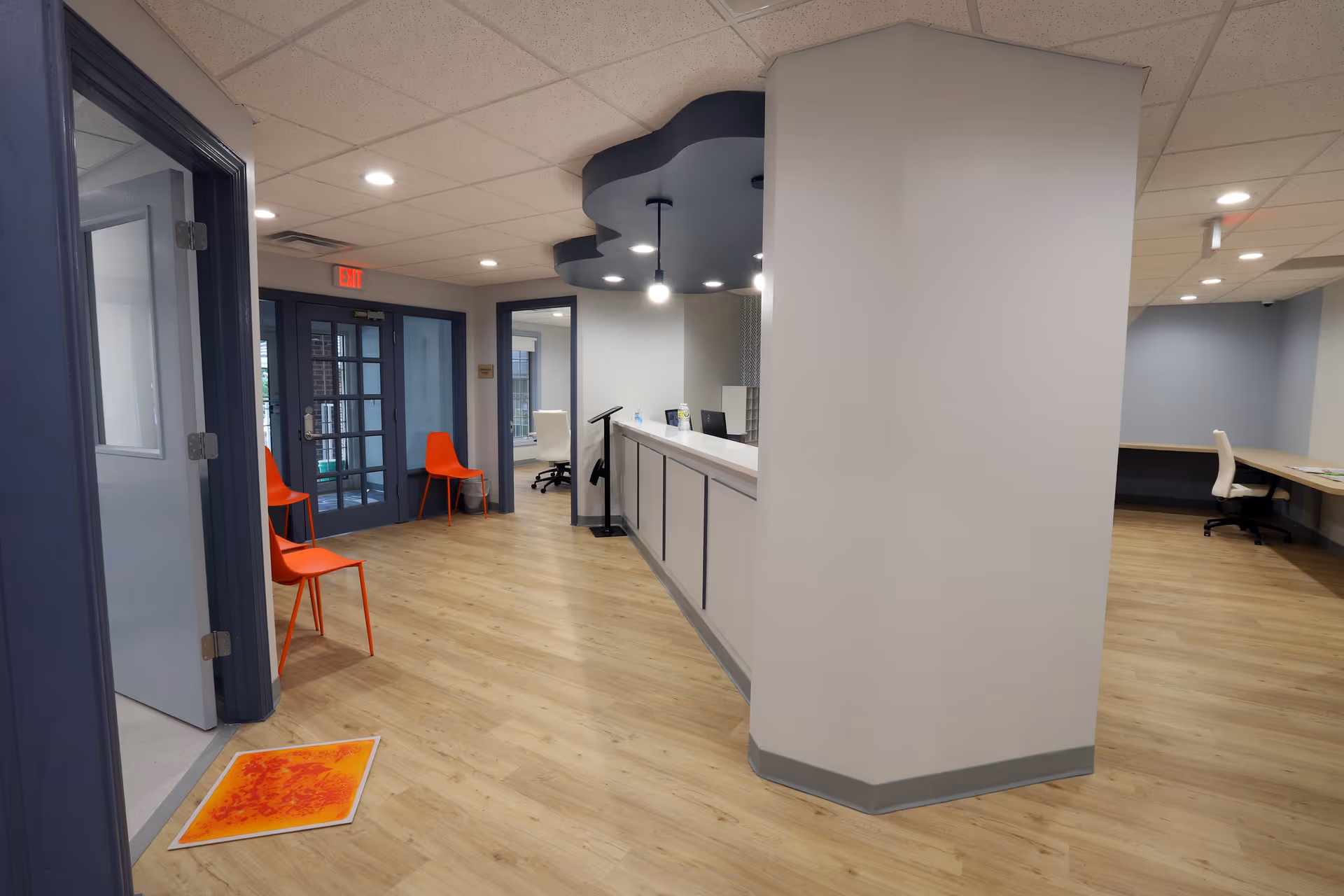 Bright reception area with a long counter, orange chairs, and blue doors in an ABA facility.