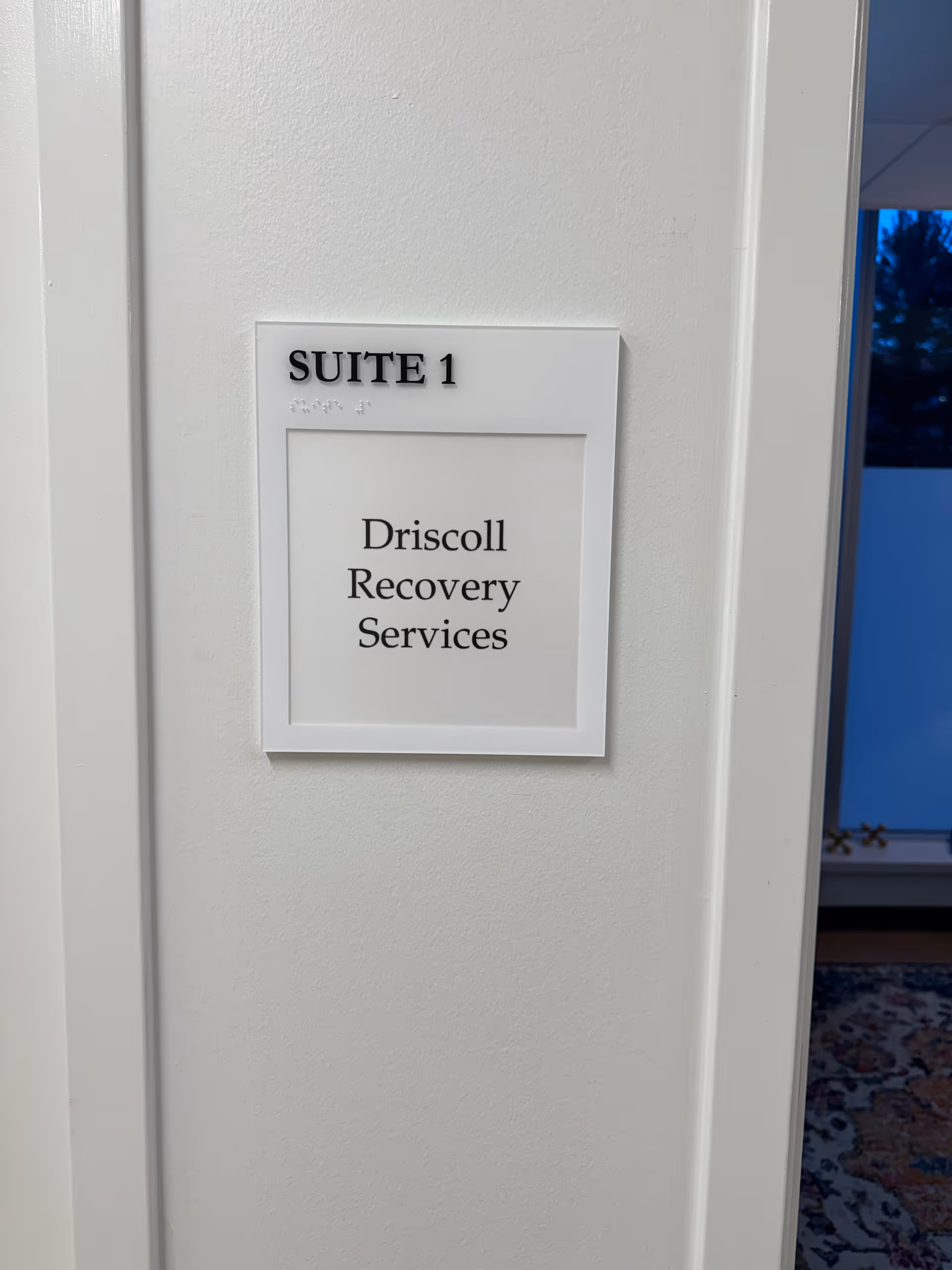 White interior wall with a suite sign and plaque reading Driscoll Recovery Services
