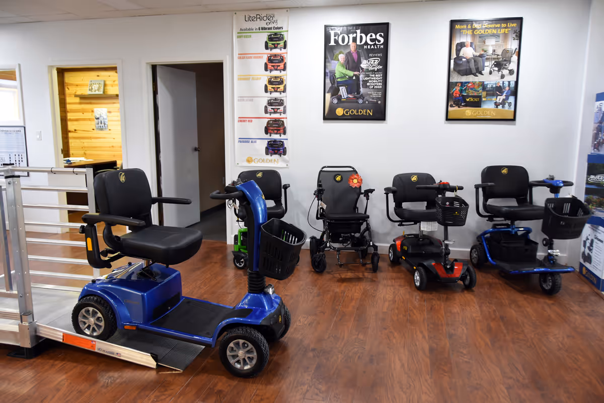 Blue mobility scooter in foreground with several other scooters and chairs inside a showroom.