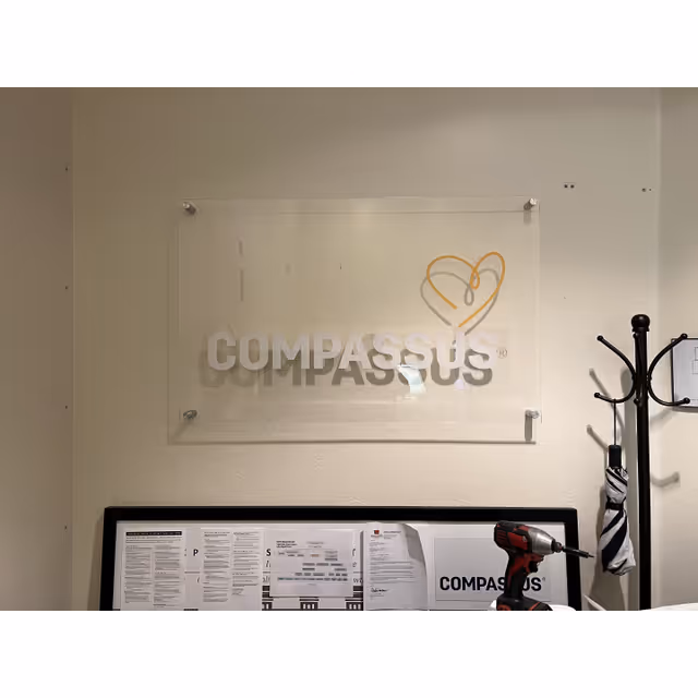 Interior wall with a Compassus sign, glass plaque, coat rack, and papers on a desk.