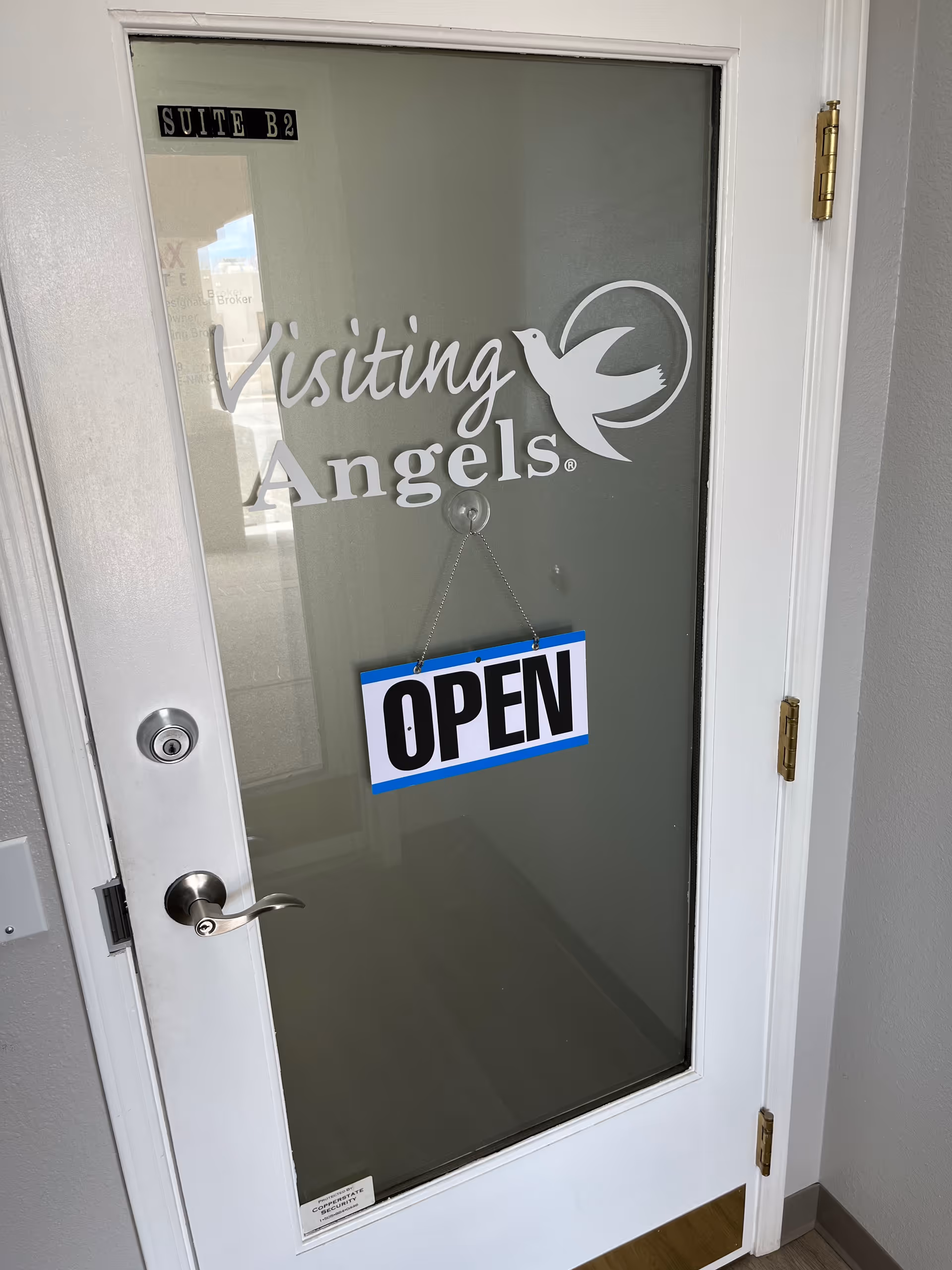 Glass door with Visiting Angels logo and OPEN sign in a hallway.