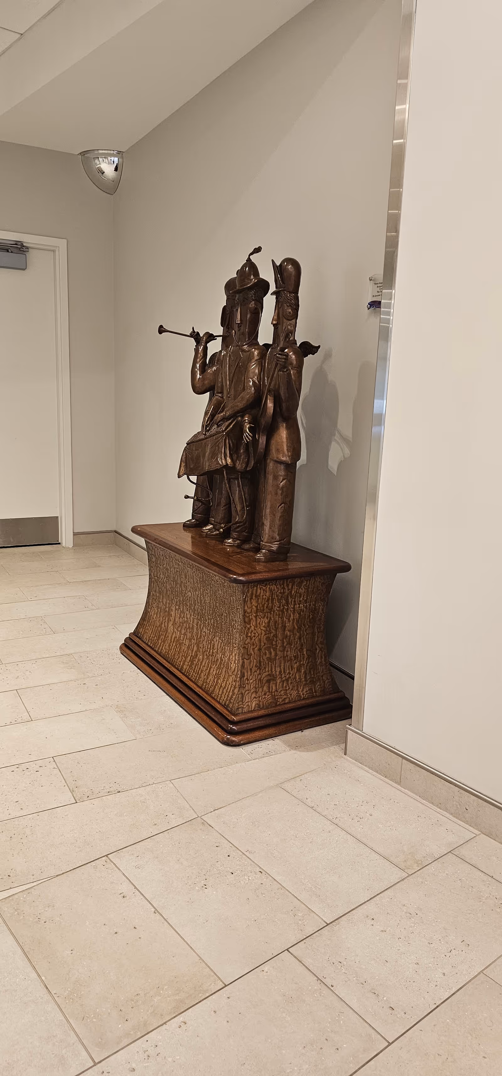 Bronze statue of three musicians on a wooden pedestal in a hallway.