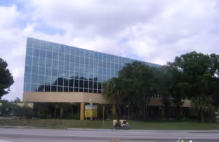 Modern glass-front building exterior with trees and a road in front.