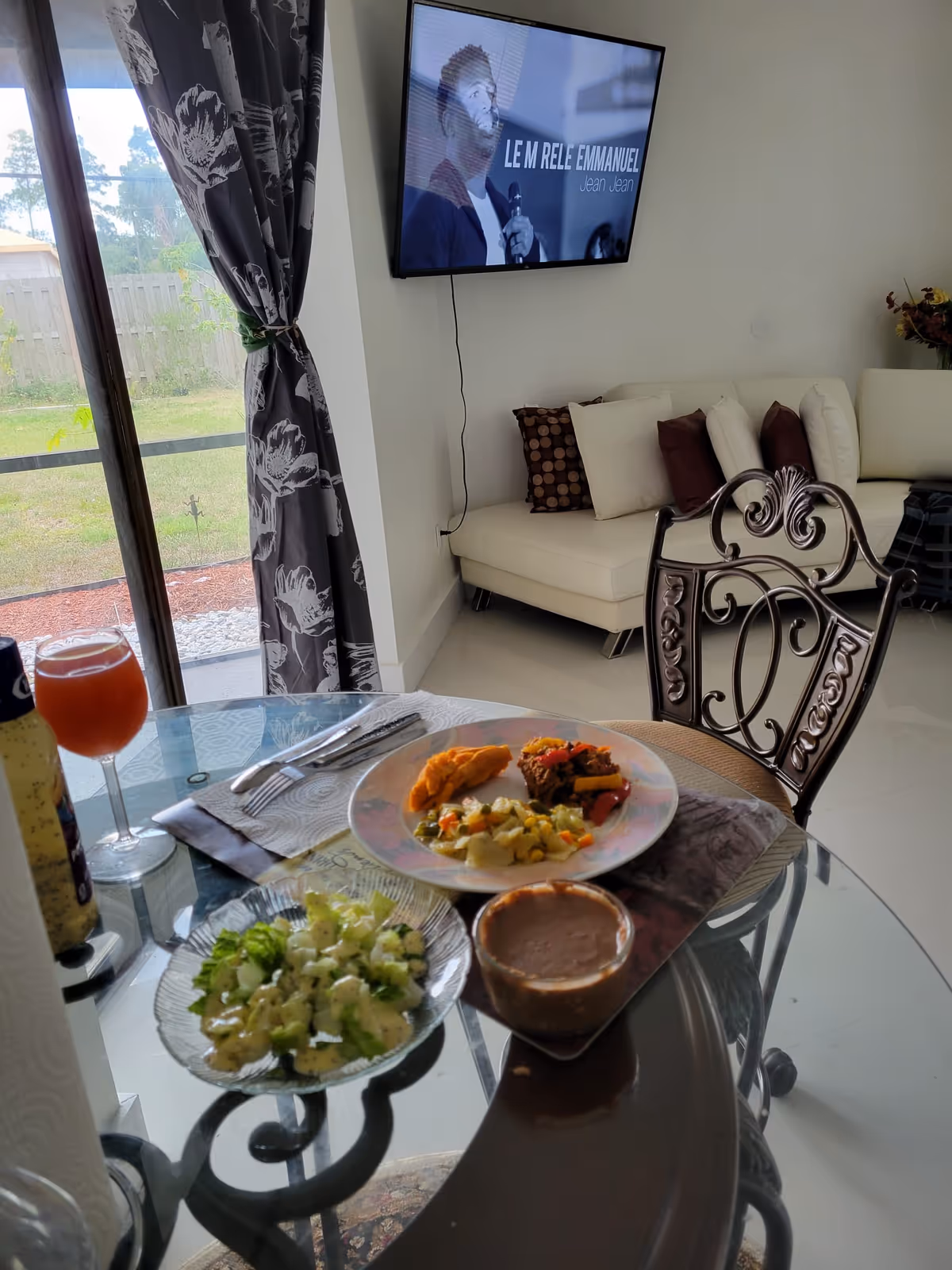 Glass dining table with plates of food, a sofa, and a mounted TV in living area.