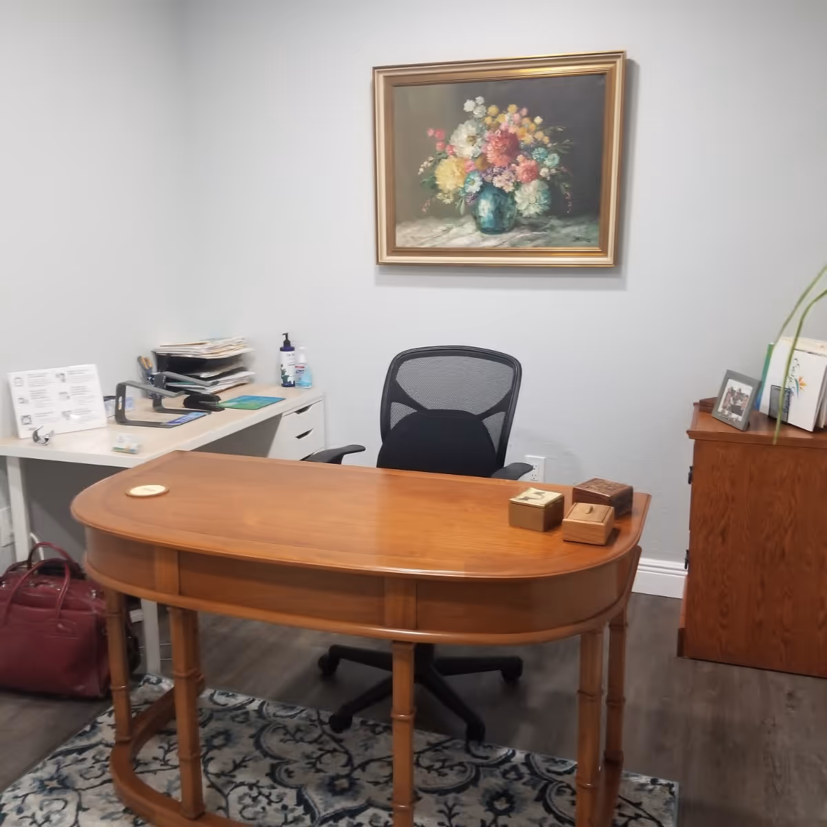 Reception desk in a small office with a chair, framed painting, and assorted paperwork.