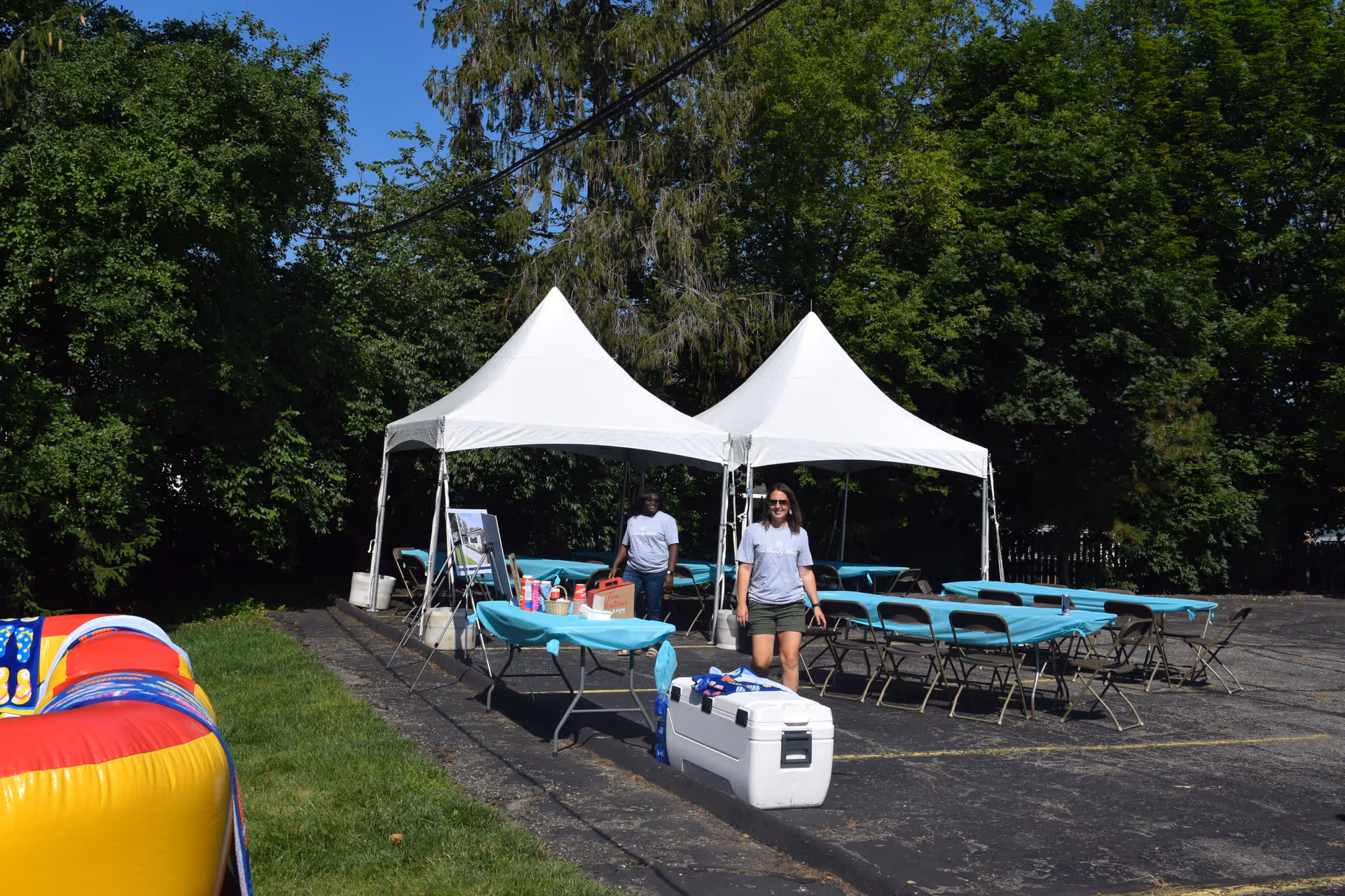 Outdoor event setup with two white tents, turquoise tables, and folding chairs.