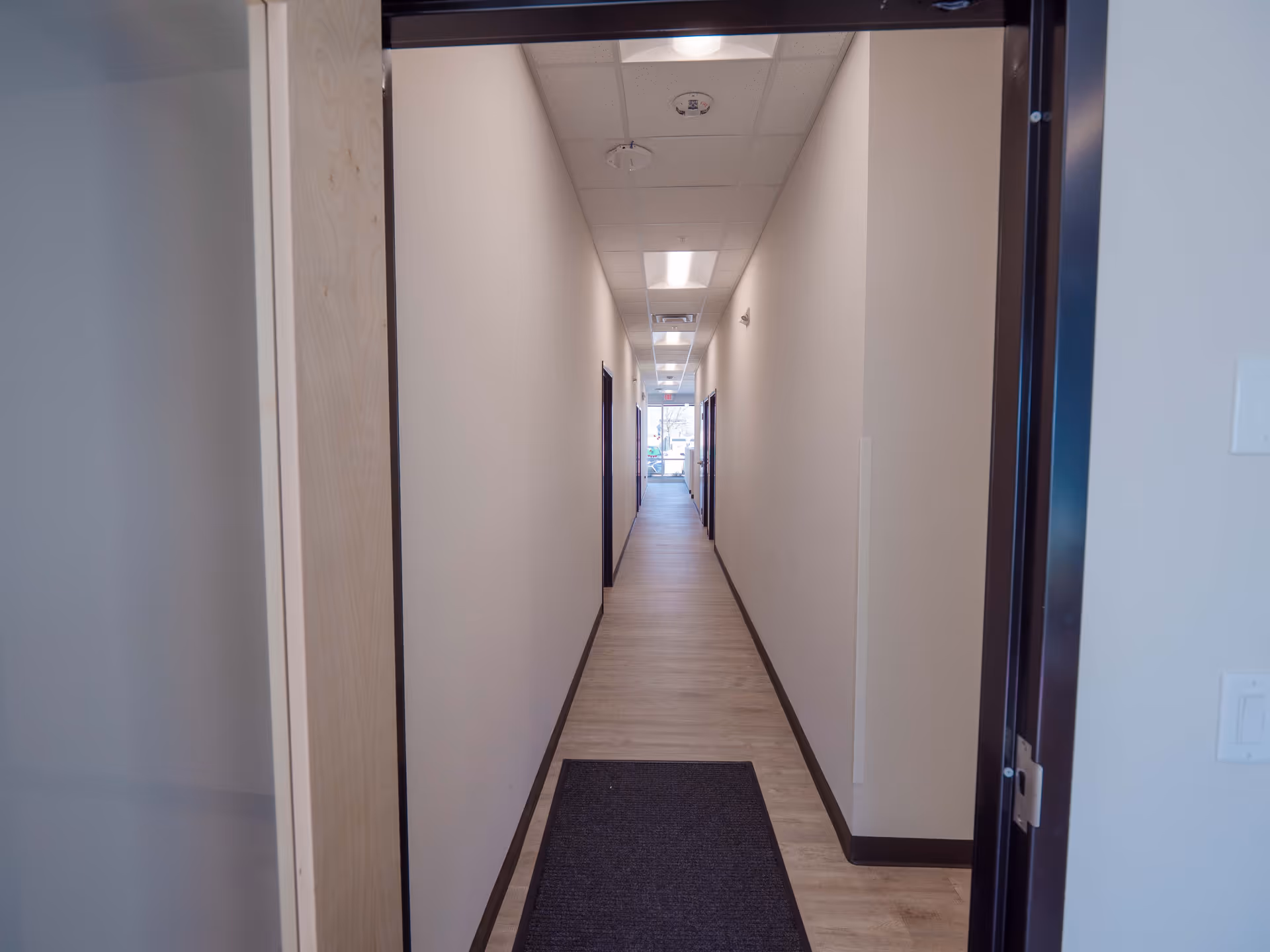 Long, empty corridor in a facility lined with doors and bright ceiling lights.