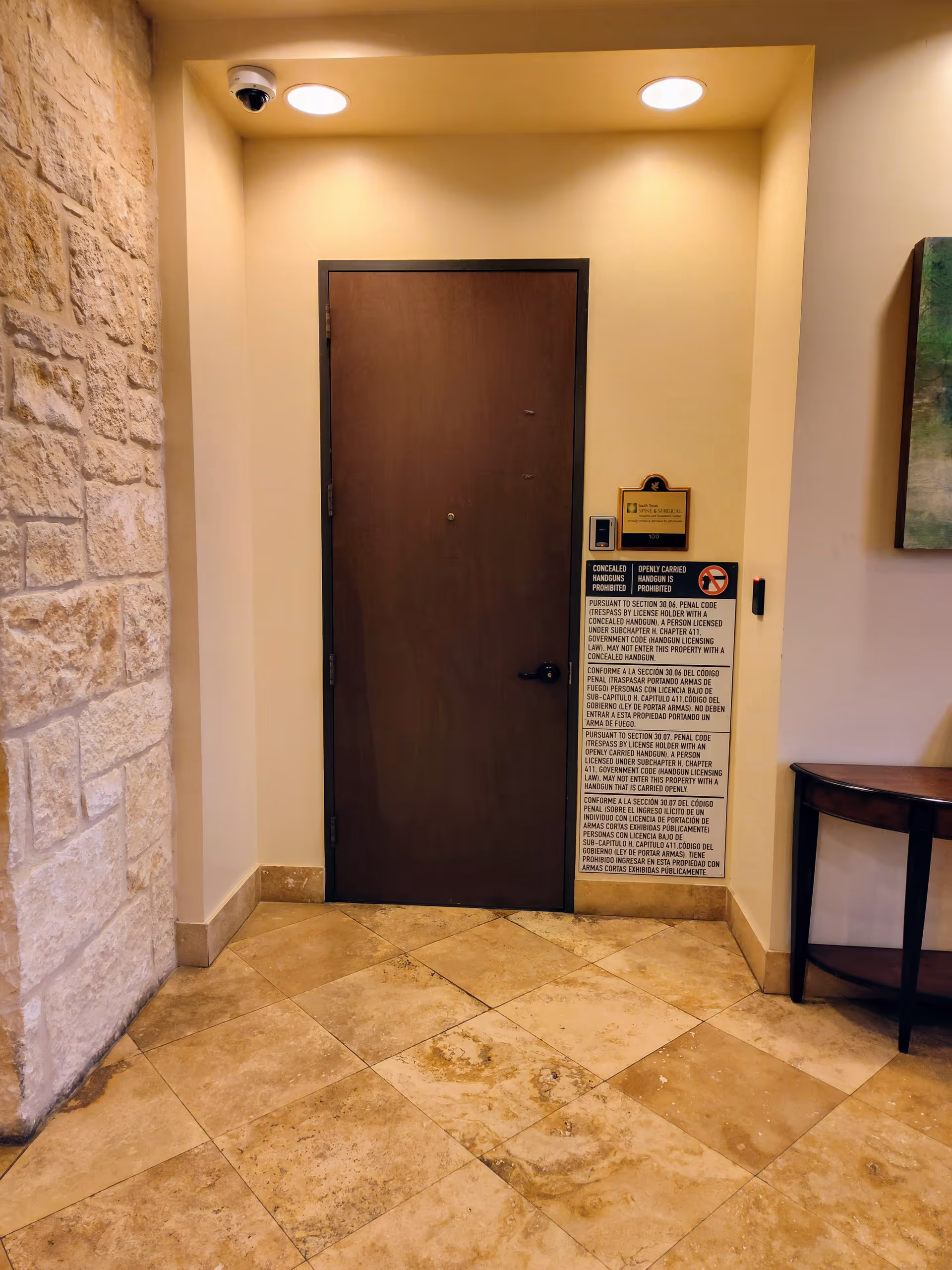 Interior corridor with a wooden door, stone wall on left, beige walls, tiled floor