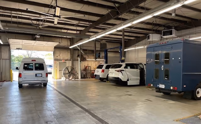 Spacious indoor vehicle maintenance area with several mobility vans parked inside.