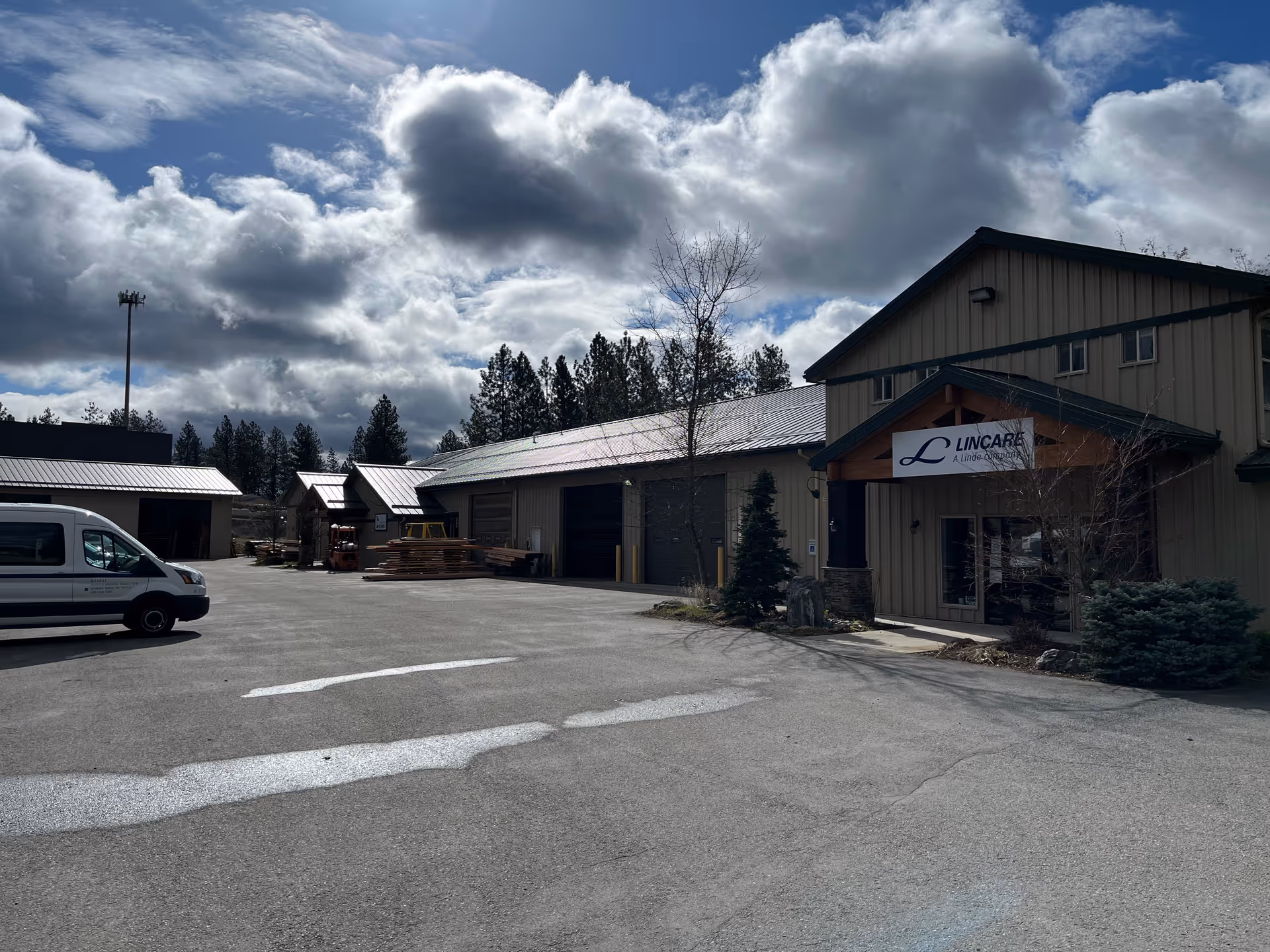 Exterior view of the LINCARE facility with a sign, parked van, and stacks of lumber.