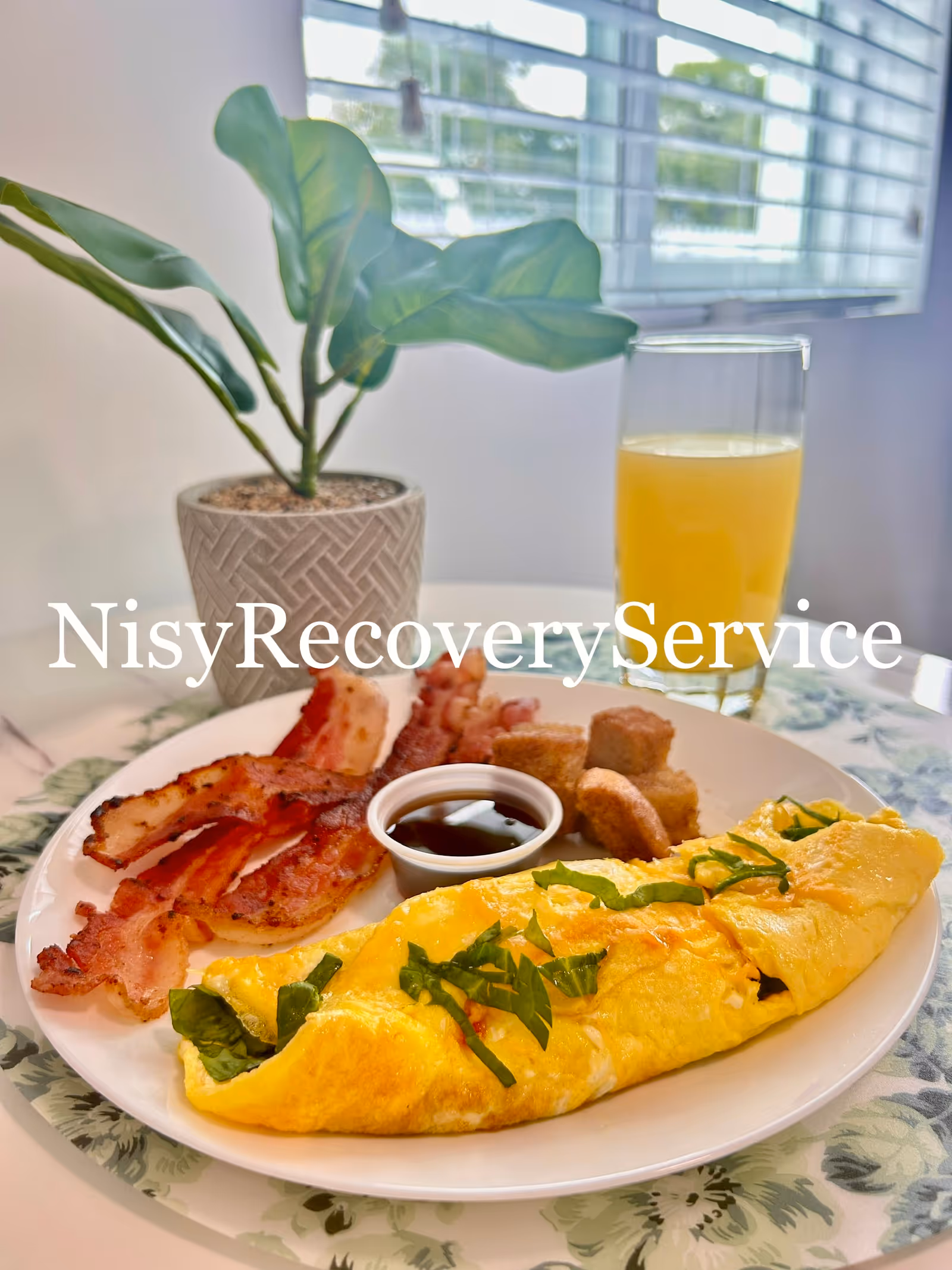Plate of breakfast with omelette, bacon, toast, orange juice; potted plant in background.