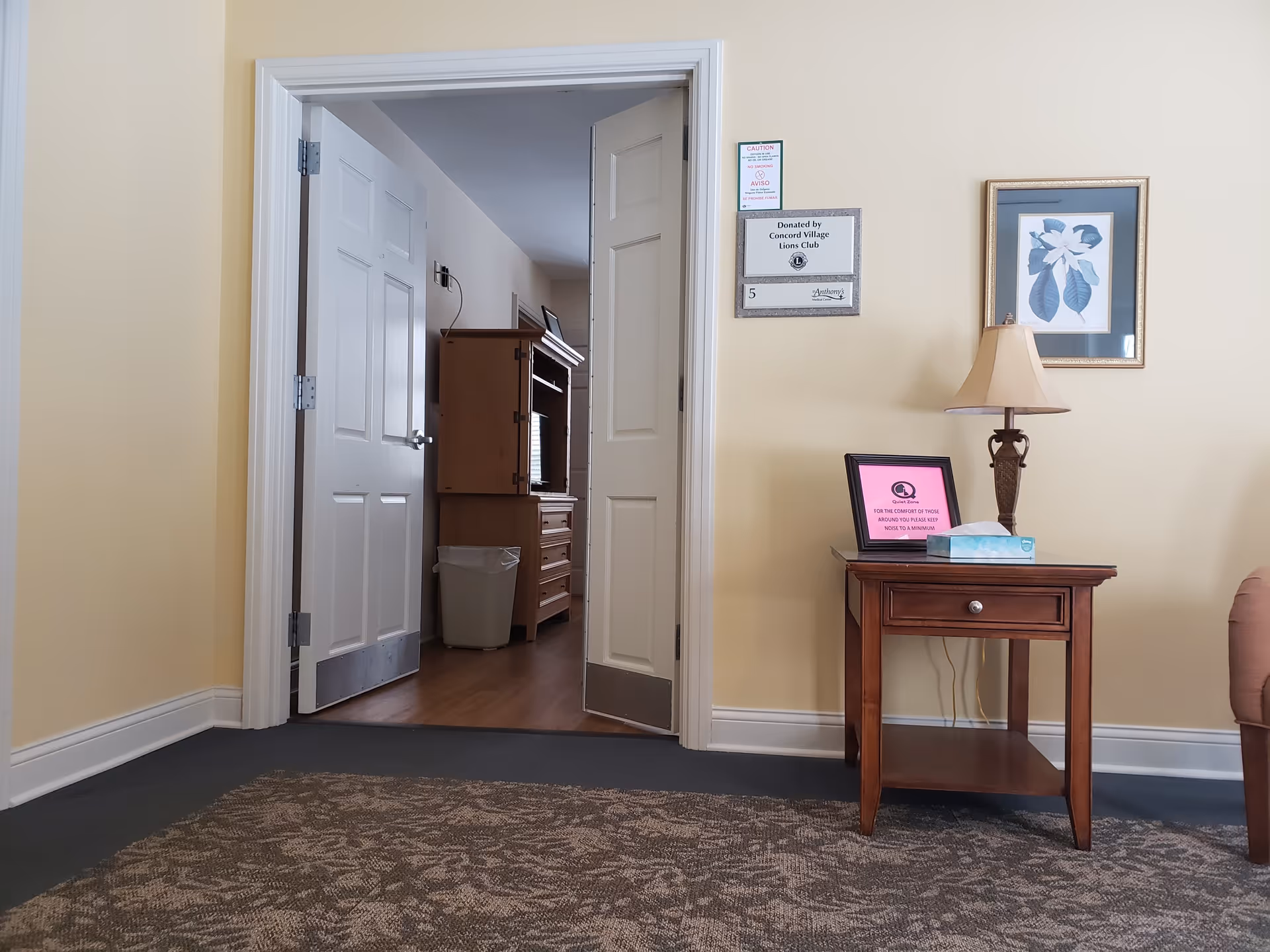 Beige interior with doorway, desk area, lamp, and framed wall art.
