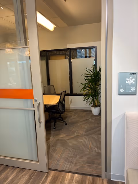 Interior office conference room with glass door, table, chairs, and a potted plant.
