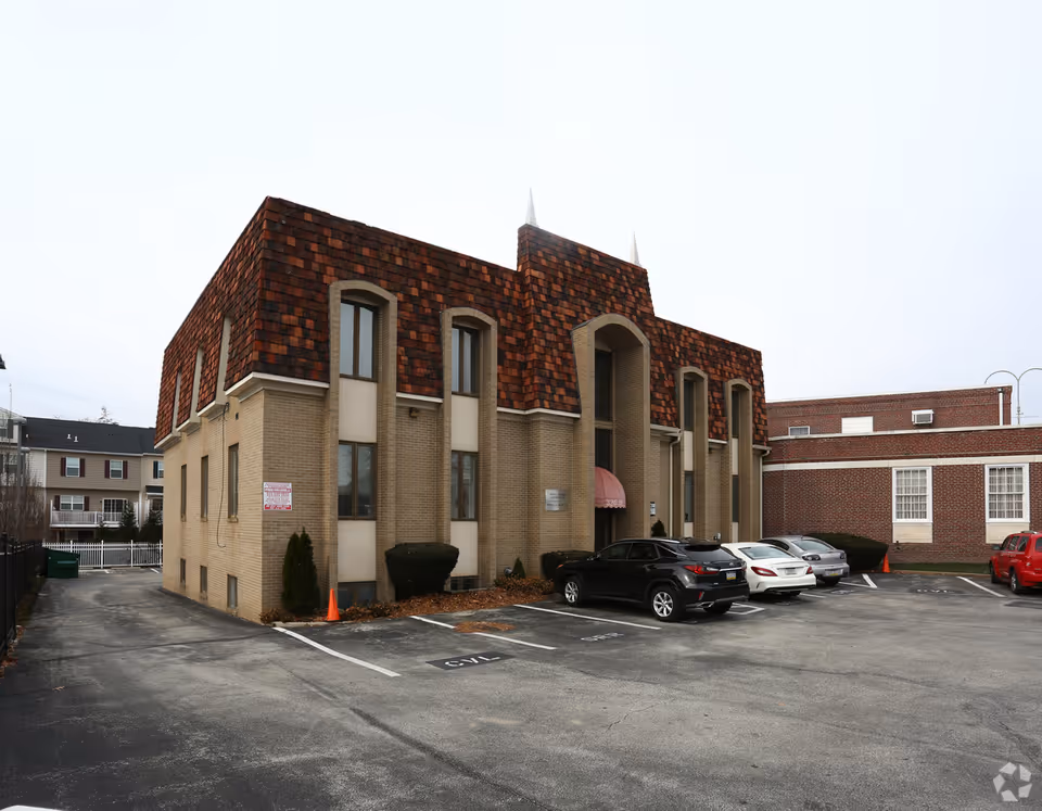 Front exterior of a brick senior care building with parked cars in the lot.