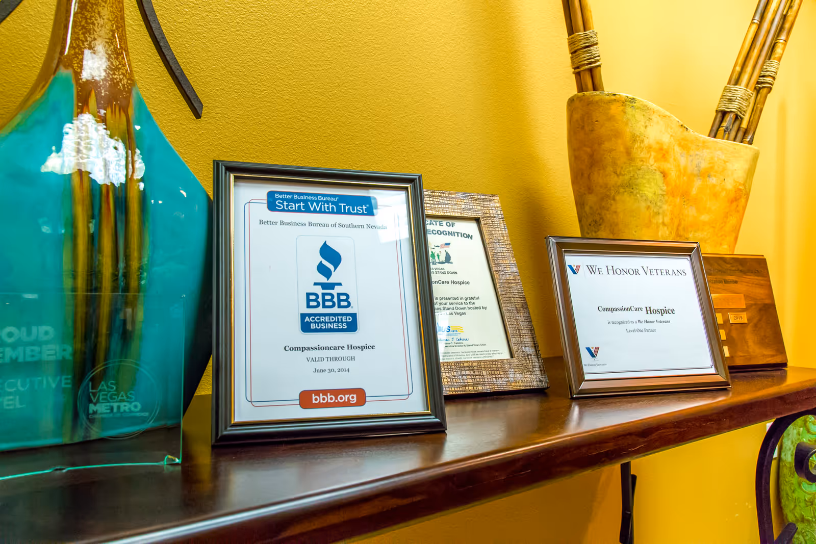 Shelf displays CompassionCare Hospice certificates and awards on a yellow wall.
