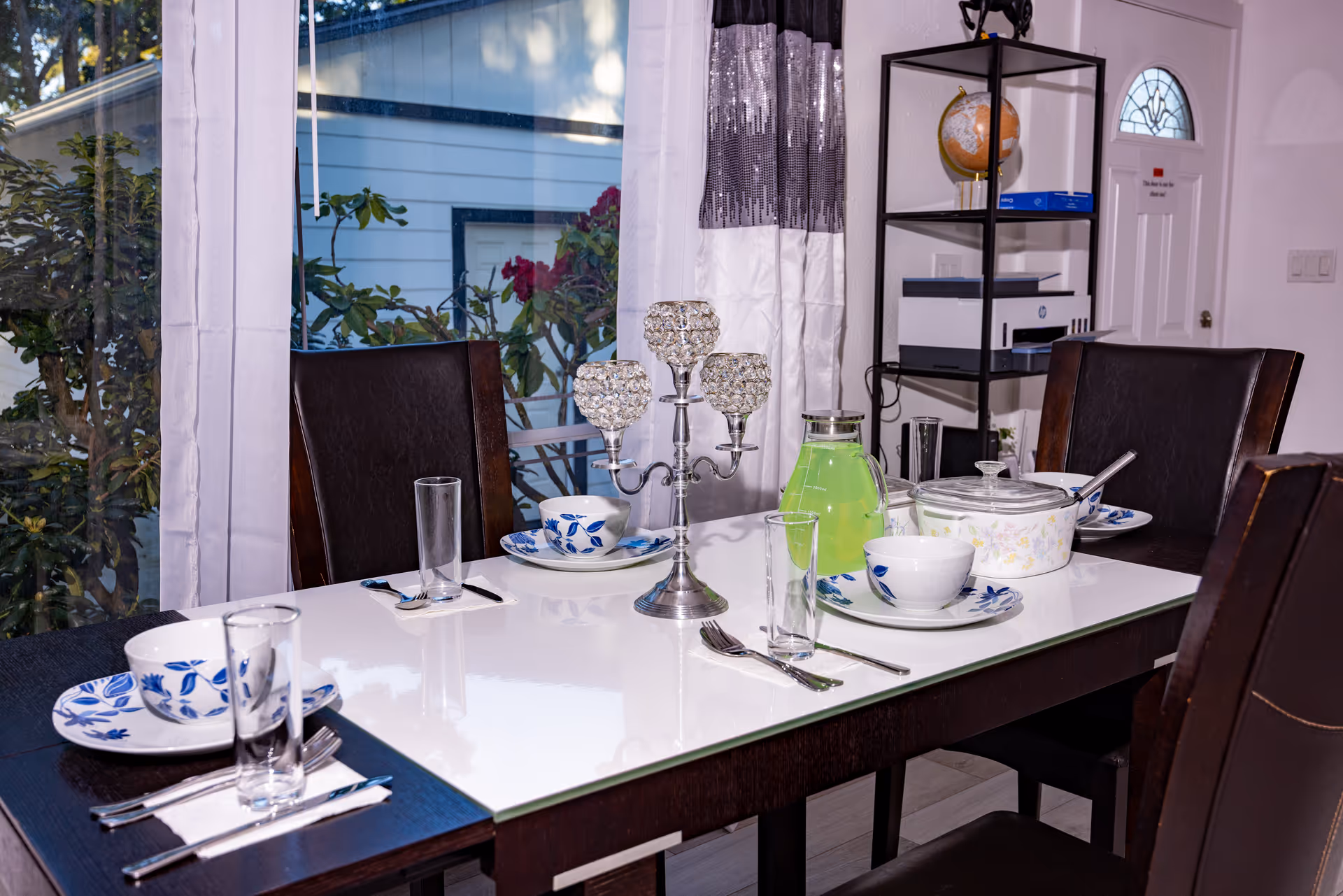 A well-set dining table with china, glasses, and a green pitcher in a bright dining room.