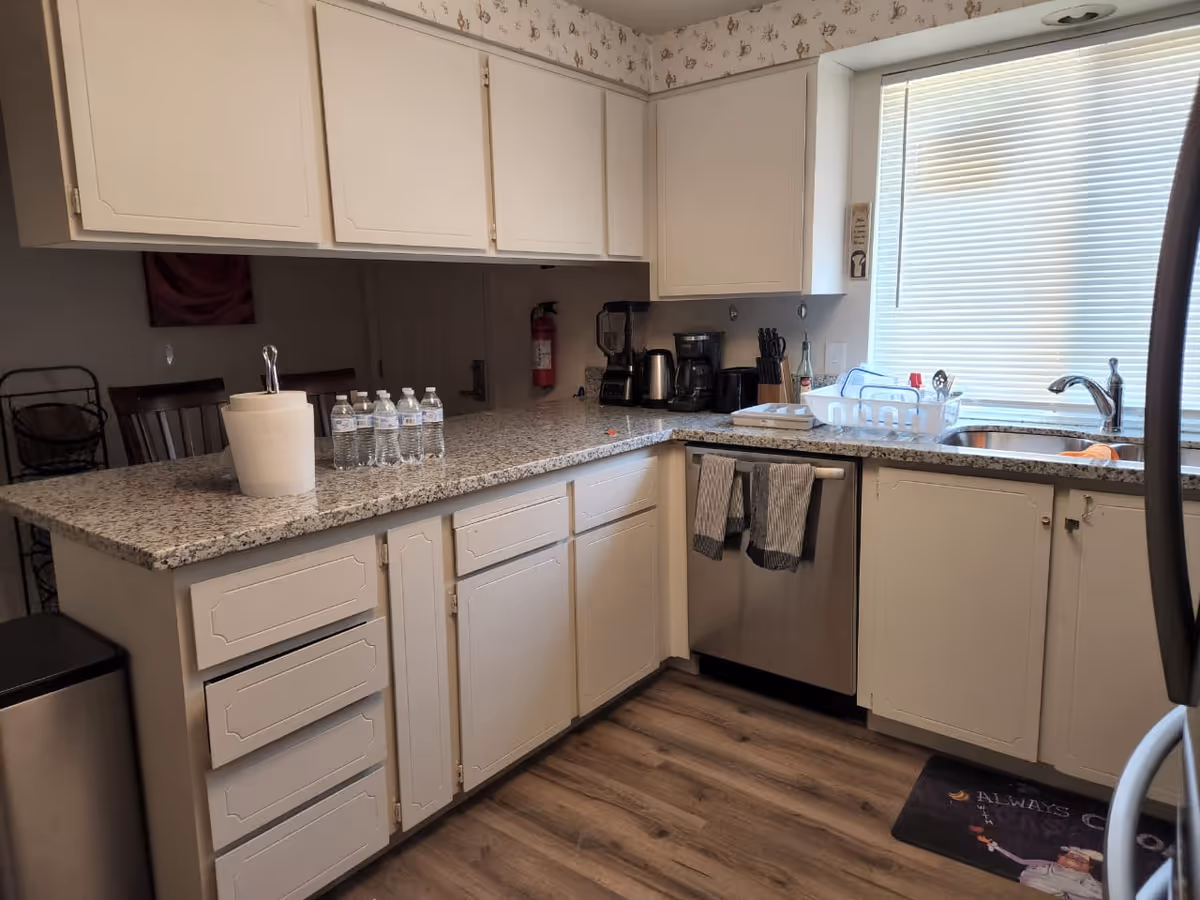 Cozy L-shaped kitchen with granite counters, white cabinets, stainless appliances, and sink.