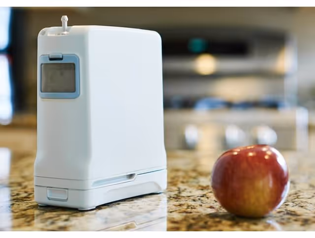 A white countertop appliance sits beside a red apple on the kitchen counter.